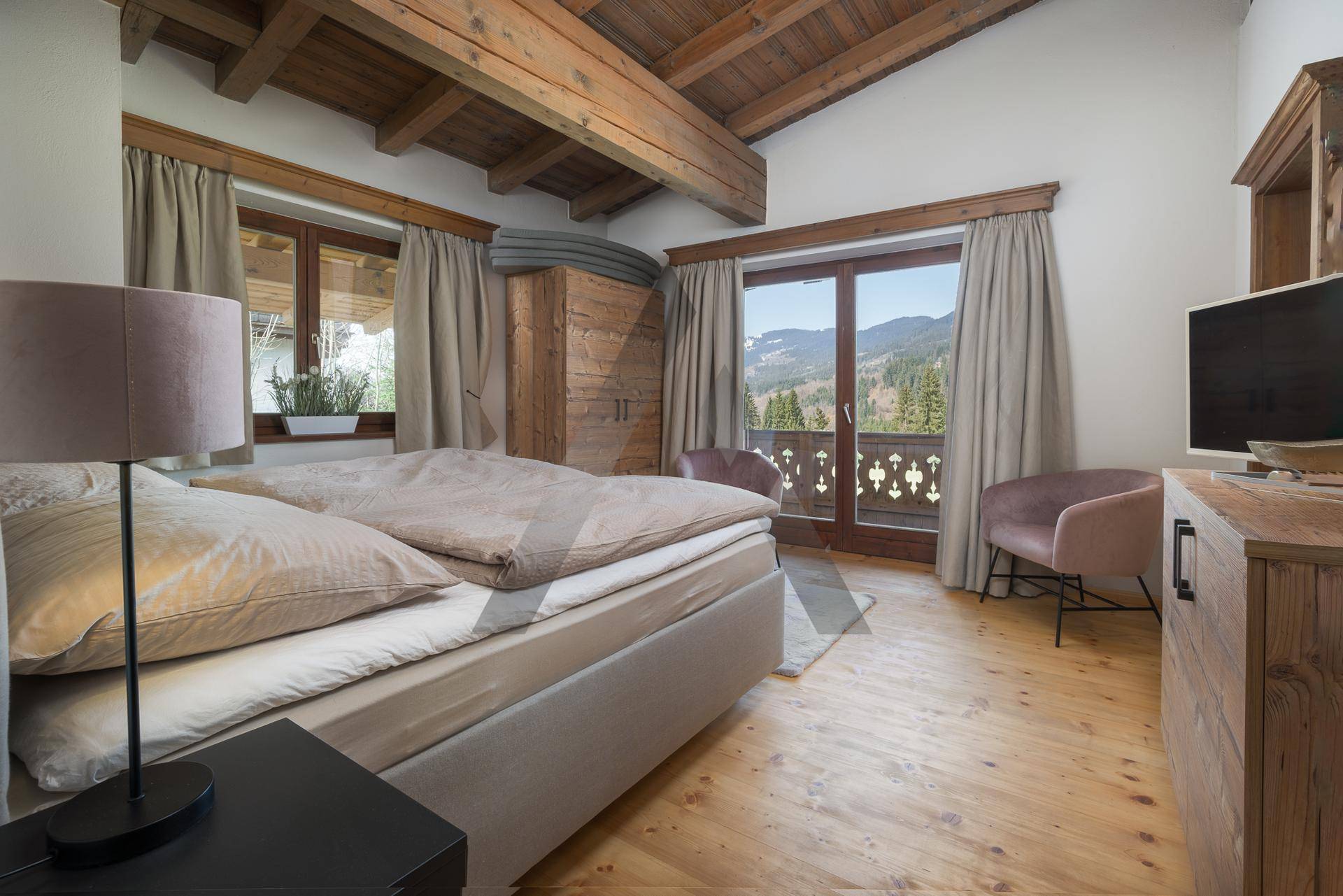 Helles Schlafzimmer mit Holzboden, Bergblick und Zugang zum Balkon mit traditionellem Geländer.