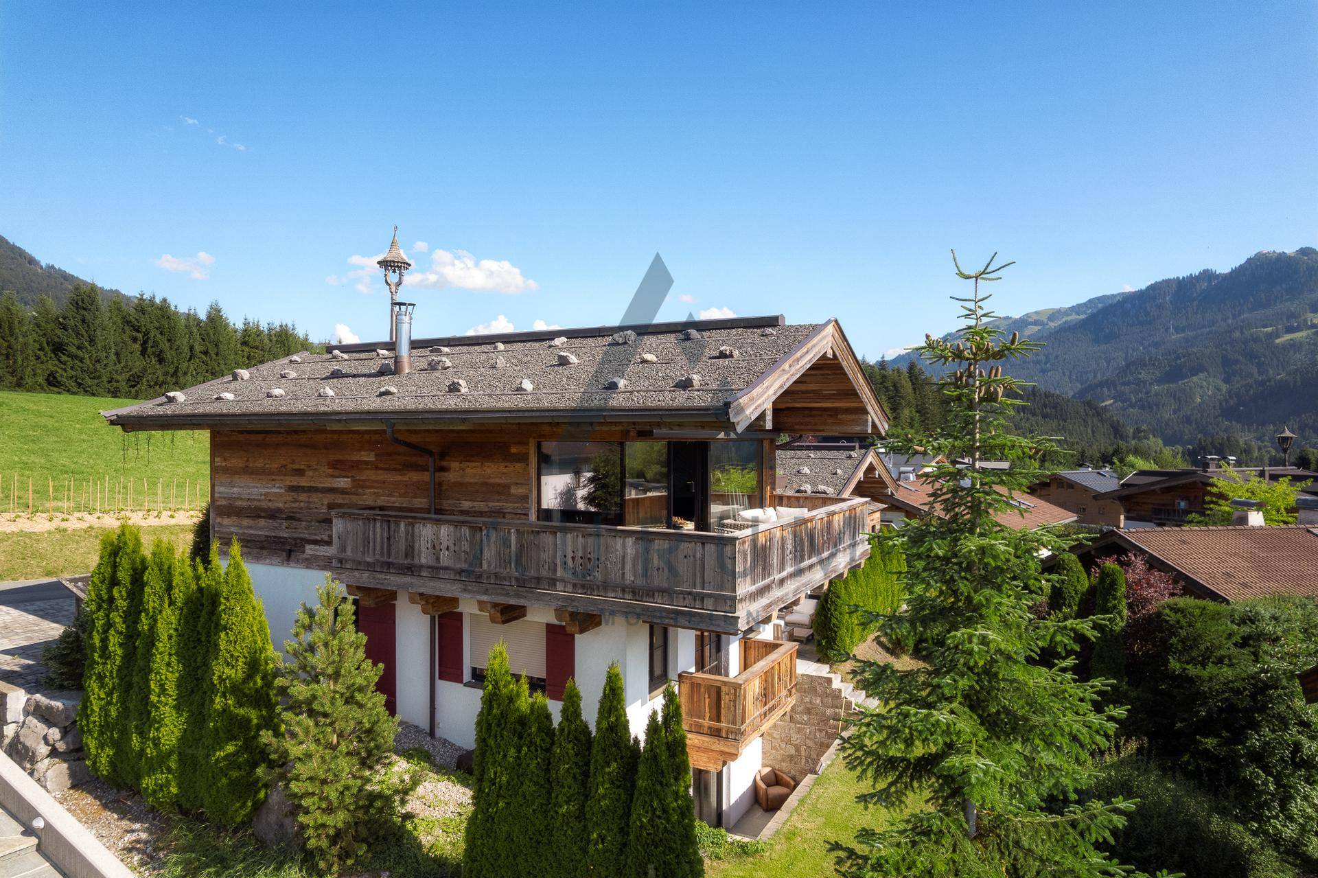 Alpines Chalet mit traditioneller Holzfassade und Balkonen, eingebettet in grüne Hügellandschaft.