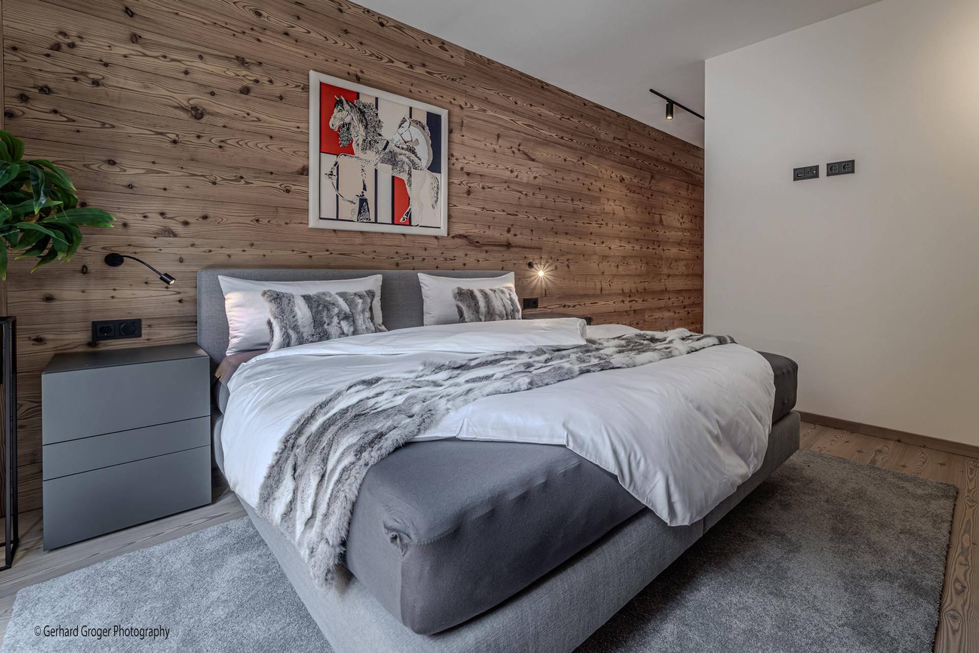 Gemütliches Schlafzimmer mit Holzwand, großem Bett und moderner Kunst.