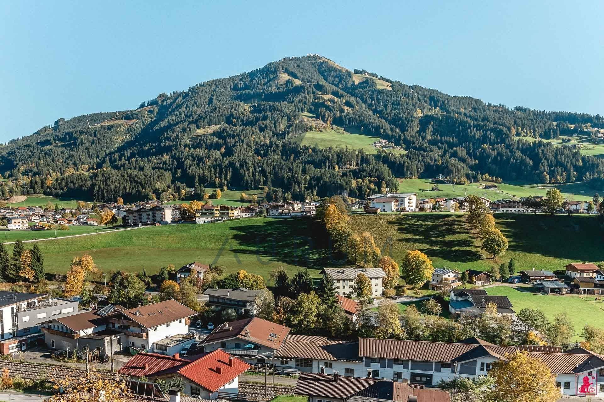 Panoramablick auf ein malerisches Dorf in einem grünen Tal, umgeben von bewaldeten Bergen.
