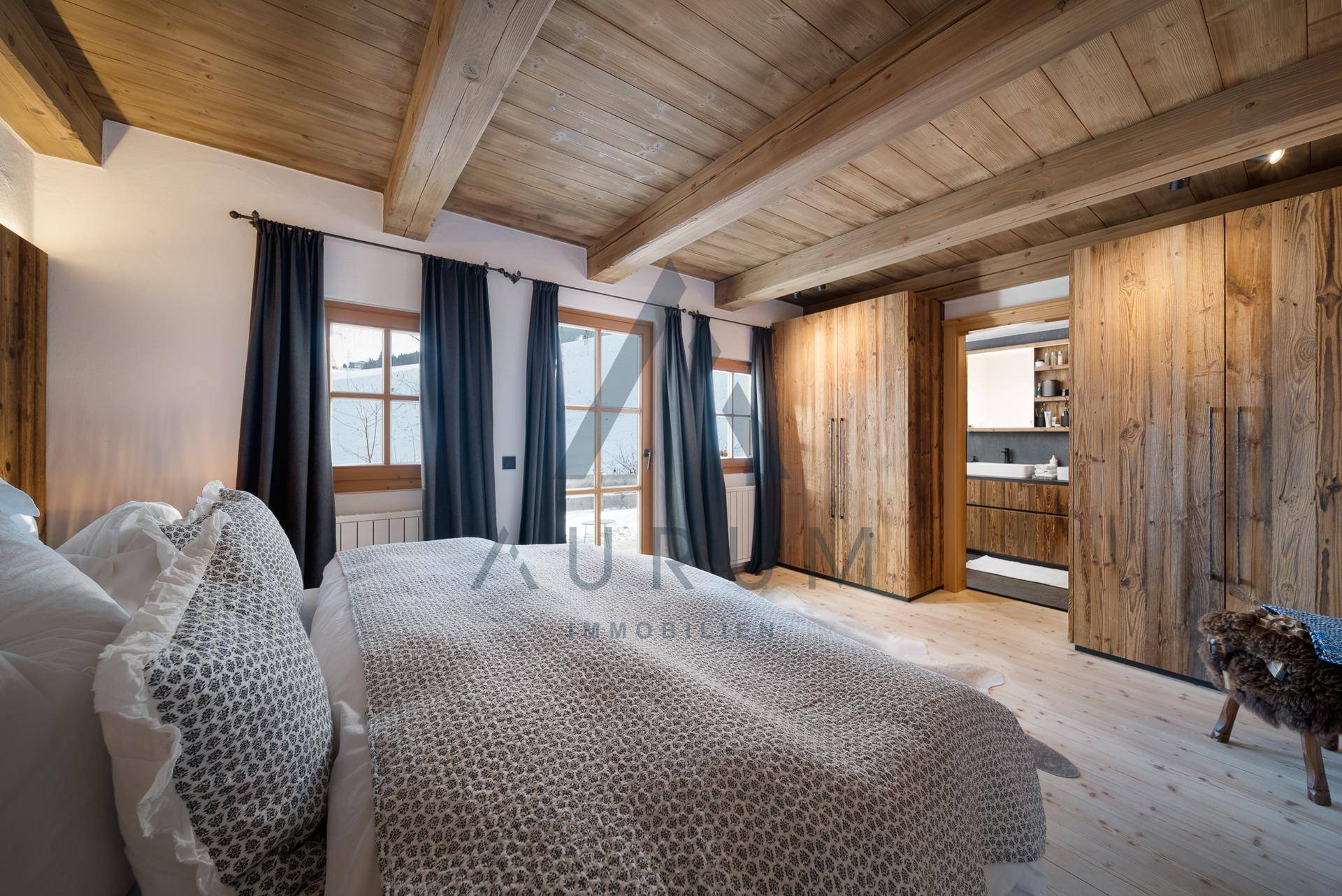 Helles Schlafzimmer mit Holzbalkendecke, Einbauschränken und Zugang zum modernen Badezimmer.