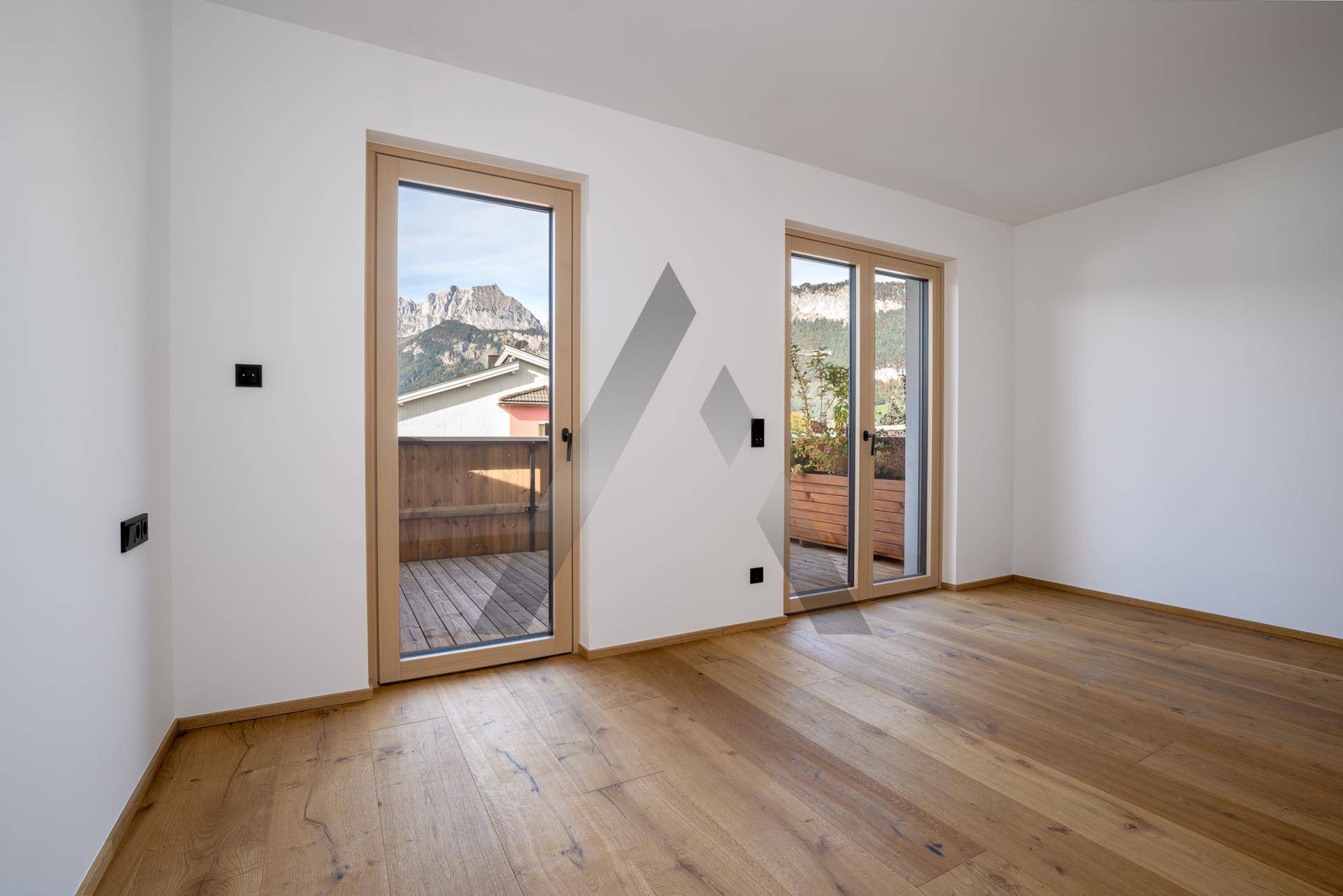 Geräumiger Wohnbereich mit Holzboden und Zugang zu einem Balkon mit Bergblick.