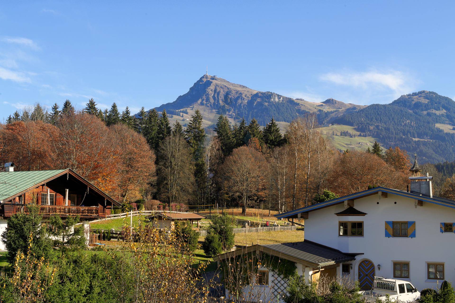 Idyllischer Blick auf die alpine Berglandschaft mit traditionellen Häusern und herbstlich gefärbten Bäumen.