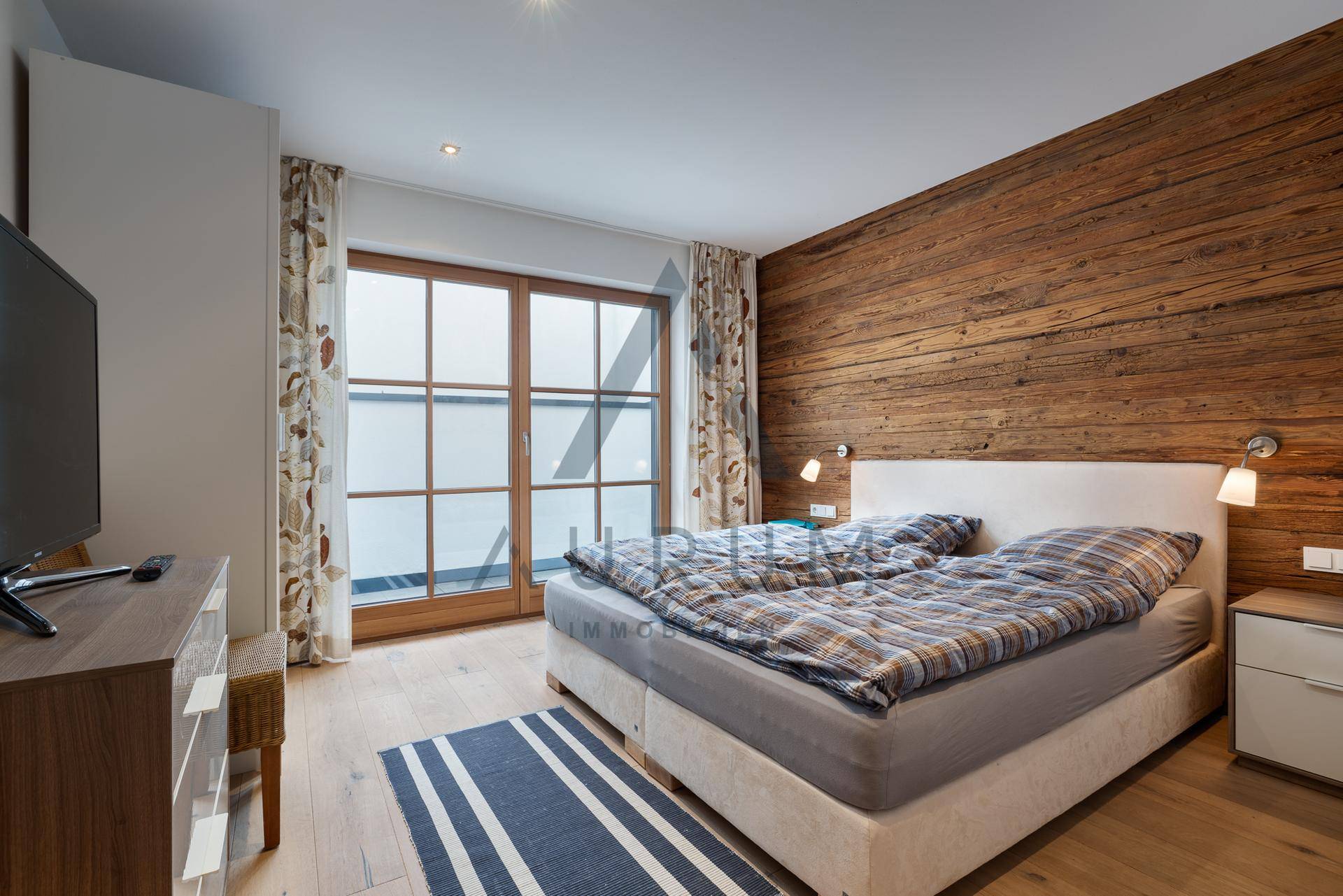 Helles Schlafzimmer mit Holzwand, Parkettboden und großem Fenster.