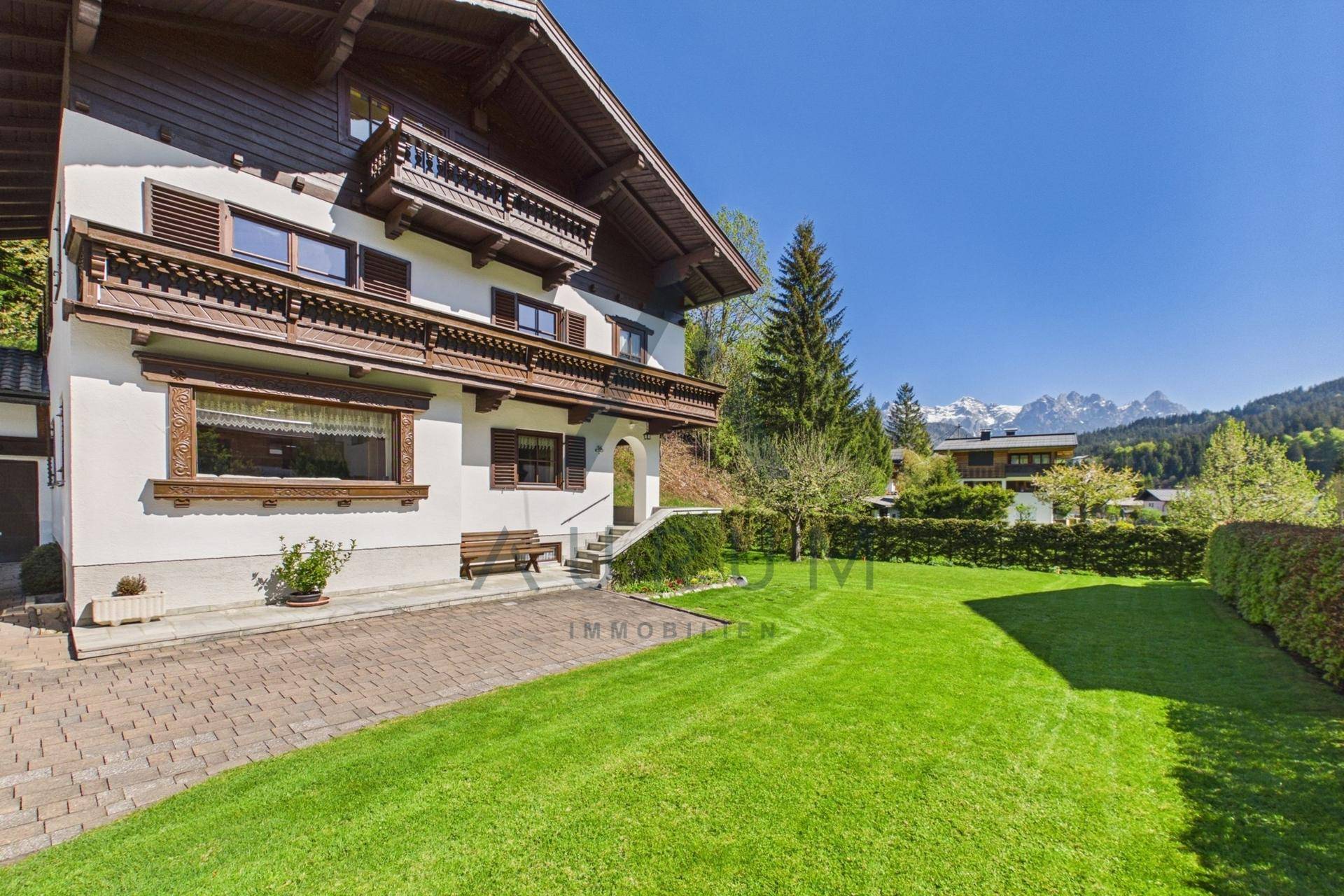 Charmantes Haus im alpinen Stil mit gepflegtem Rasen und Bergblick an einem sonnigen Tag.