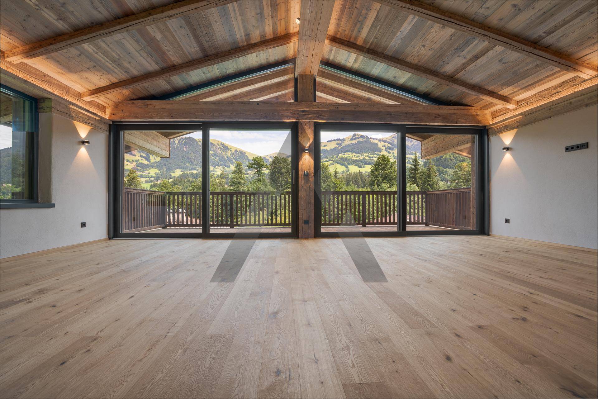 Geräumiger Wohnbereich mit Holzbalkendecke, Eichenparkett und Panoramafenstern mit Bergblick.