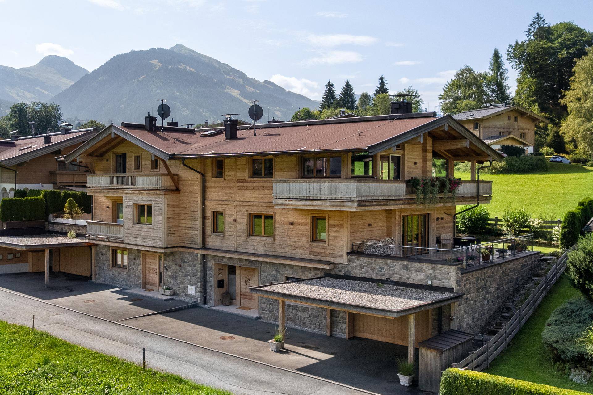 Attraktives Holzhaus mit Steinfassade, mehreren Balkonen und Carport in alpiner Umgebung.