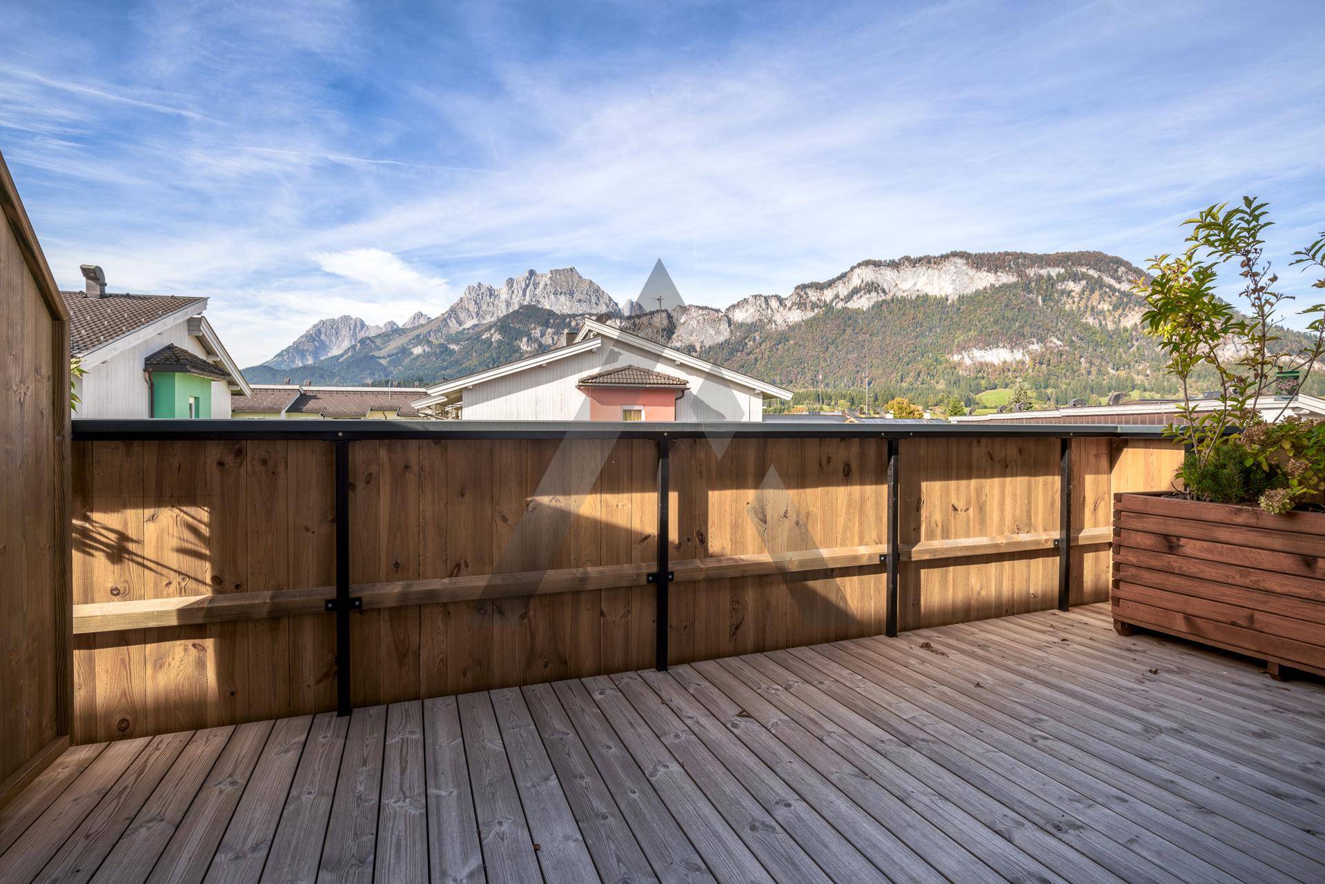 Sonniger Balkon mit Holzboden und Holzzaun, bietet einen weiten Blick auf die Berge.