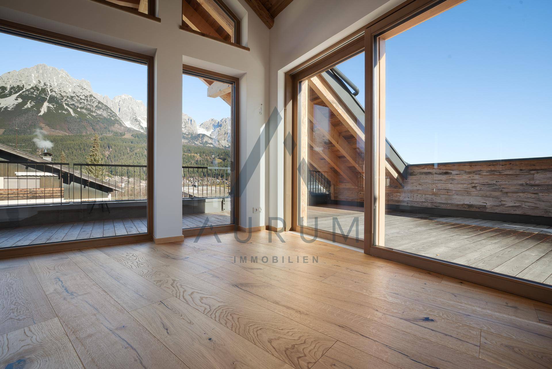 Heller Wohnraum mit Holzboden und großen Fensterfronten, die einen weiten Bergblick und Terrassenzugang bieten.