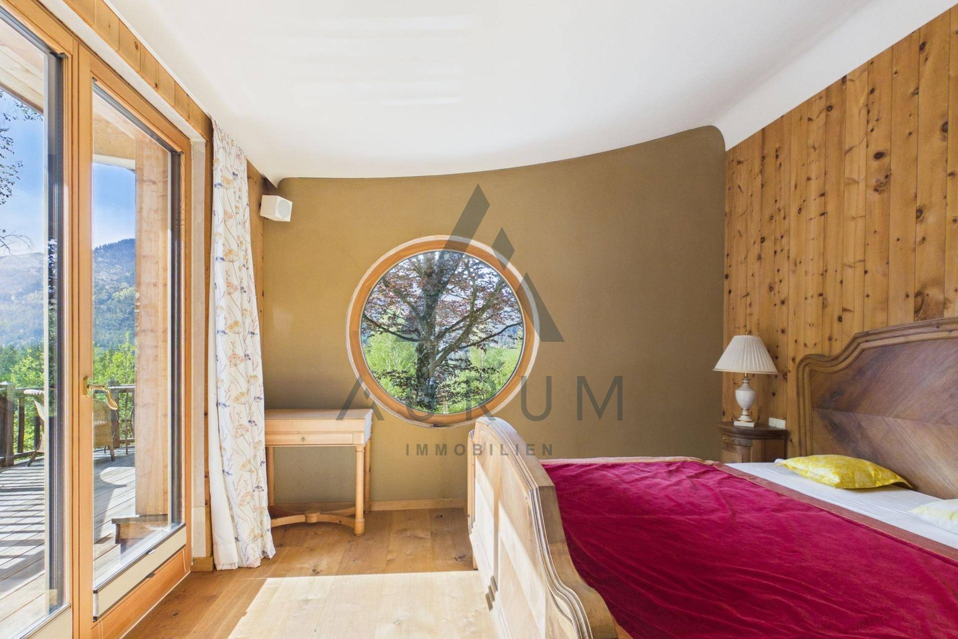 Schlafzimmer mit Holzbett, rundem Fenster und direktem Zugang zum Balkon mit Bergblick.