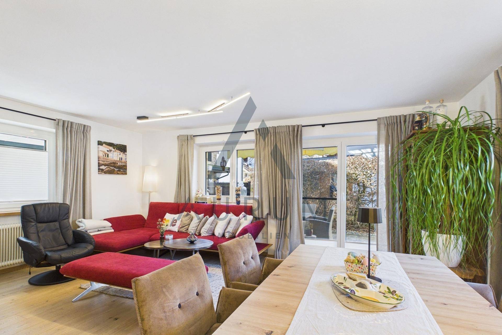 Gemütlicher Wohn- und Essbereich mit rotem Sofa, Holzboden und Blick ins Grüne.