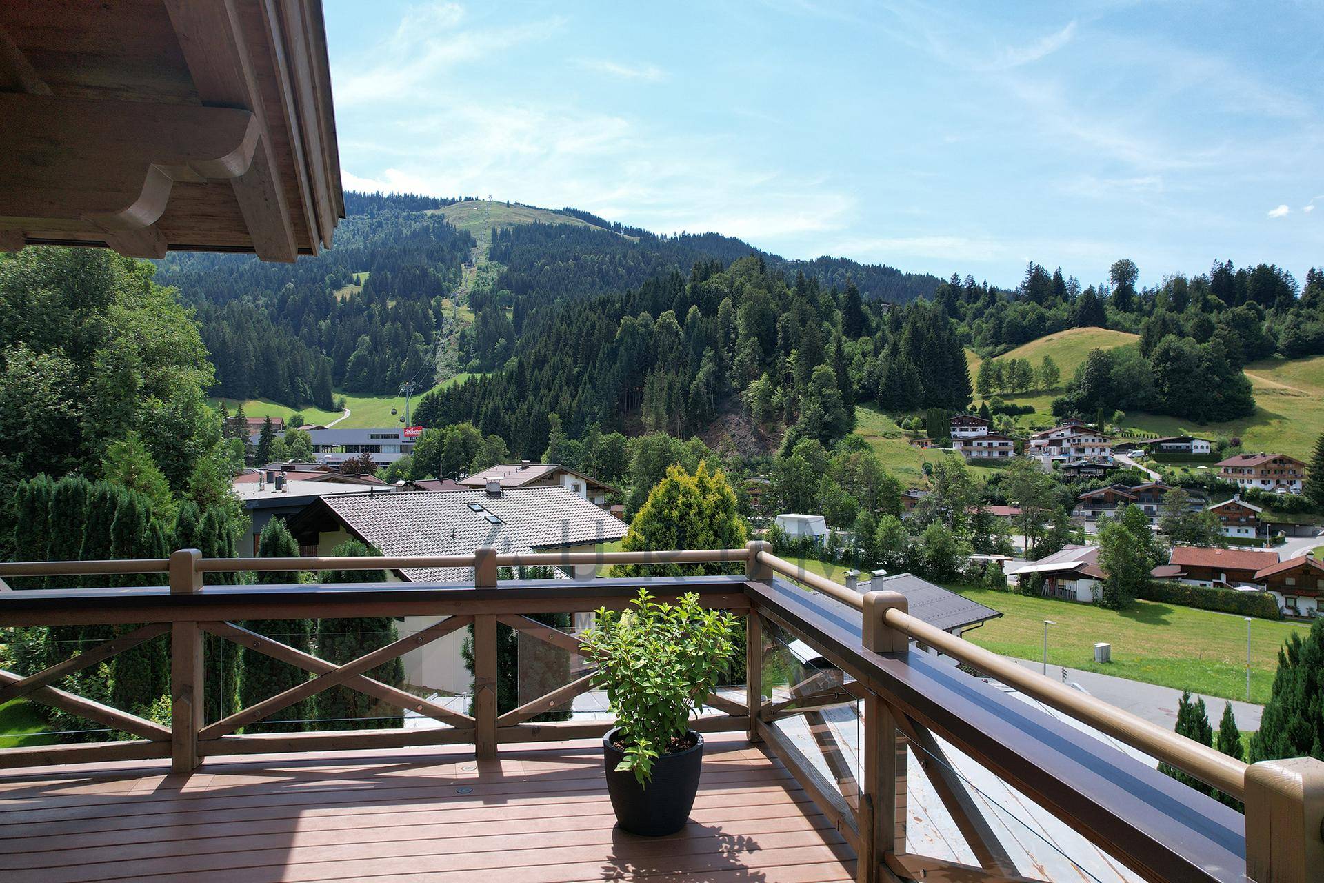 Balkon mit Holzboden und weitem Blick über die grüne Landschaft und die umliegenden Häuser.