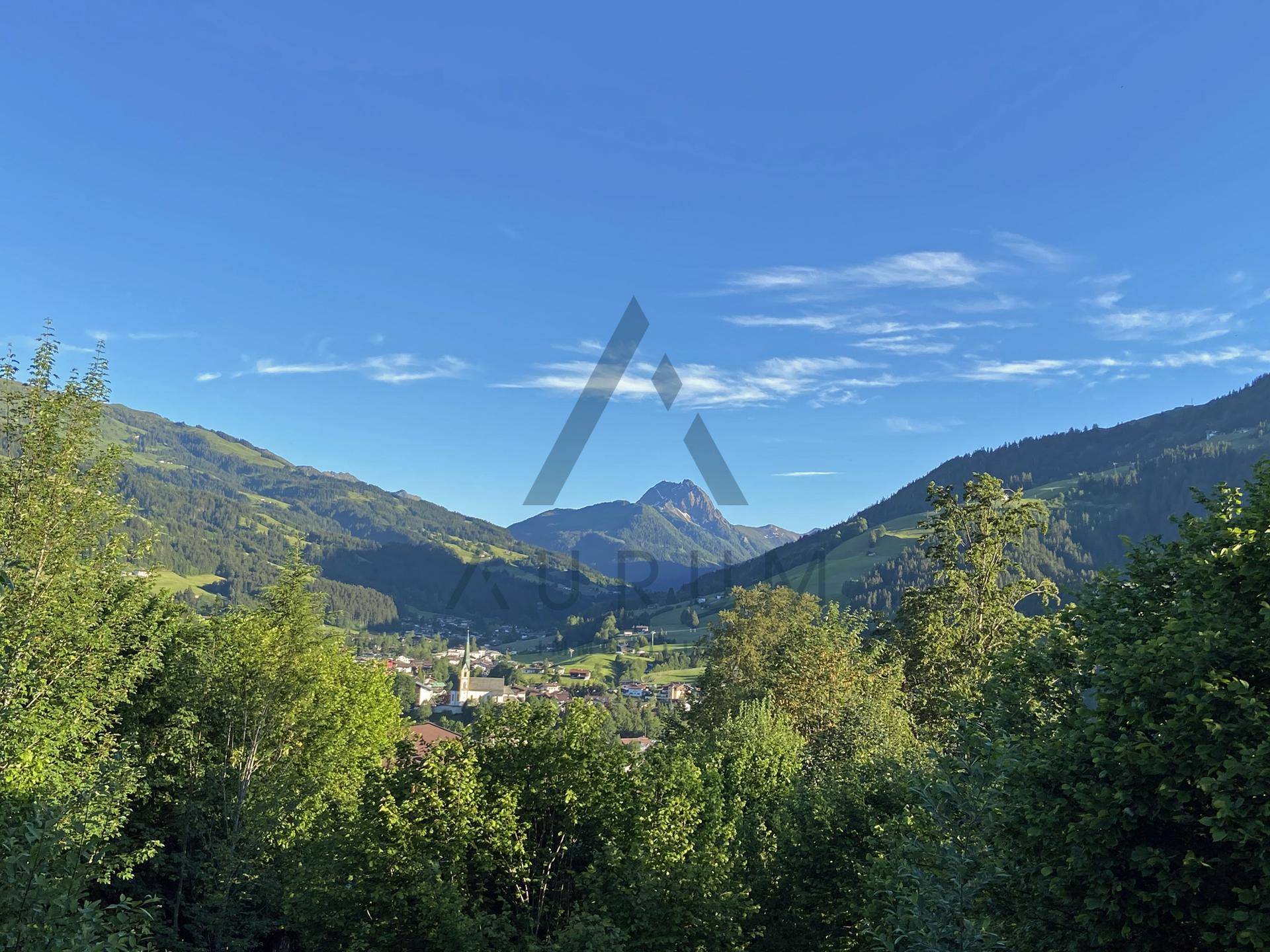 Panoramablick über ein grünes Tal mit einem Dorf und majestätischen Bergen unter blauem Himmel.