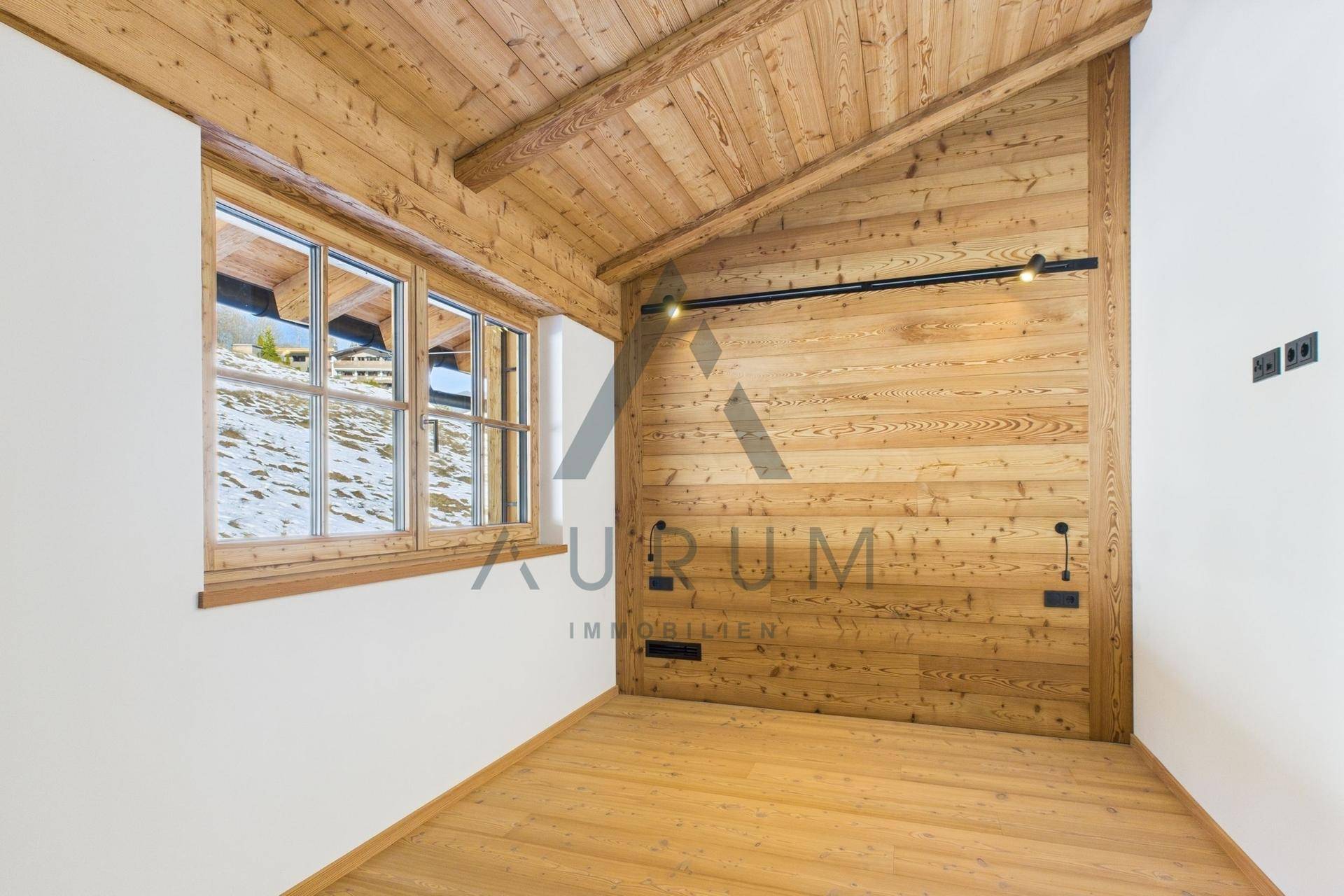 Leerer Raum mit Holzwänden, Dachschräge und Fenster mit Blick auf eine verschneite Landschaft.