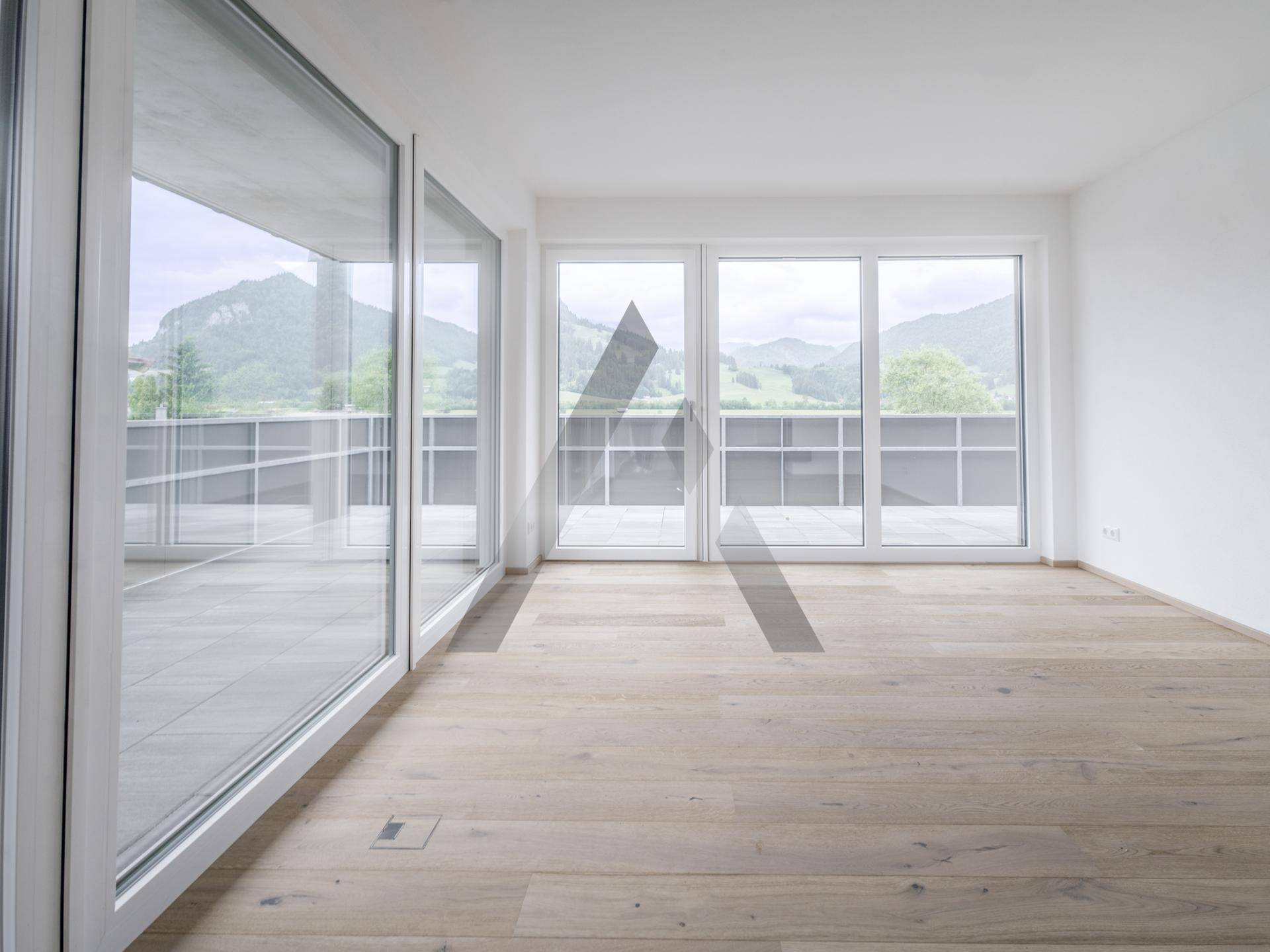 Helles Wohnzimmer mit Holzboden und raumhohen Fenstern, die einen weiten Blick auf die Berge bieten.