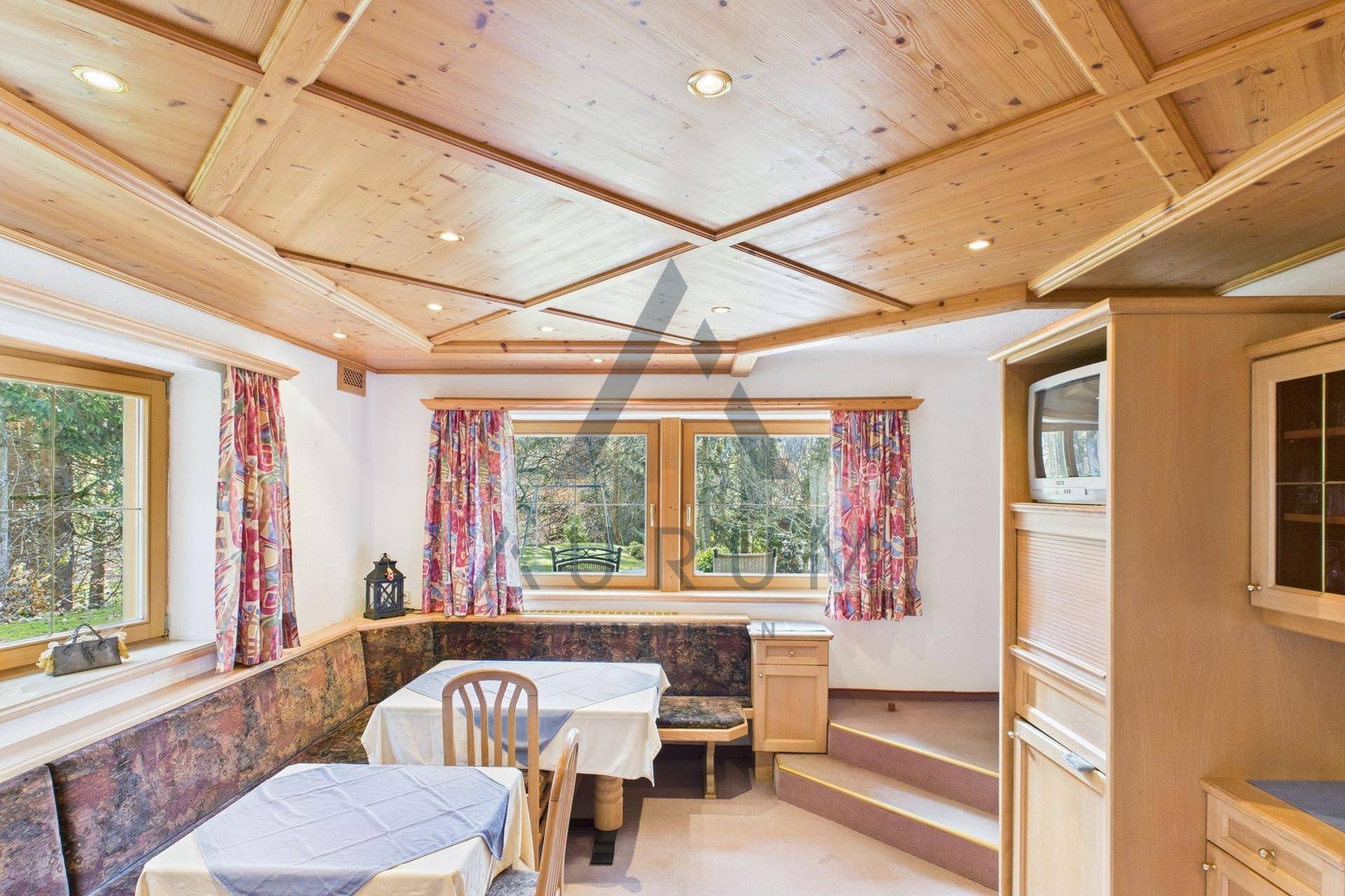 Traditionelle Küche mit Holztäfelung, Essbereich und Blick ins Grüne durch die Fenster.