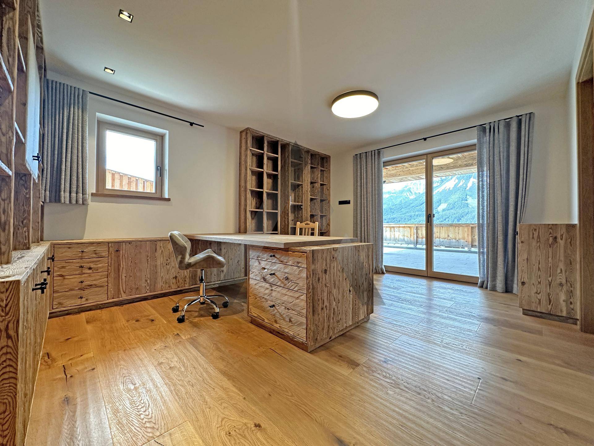 Geräumiges Büro mit Holzboden, maßgefertigten Möbeln und Zugang zur Terrasse mit Bergblick.
