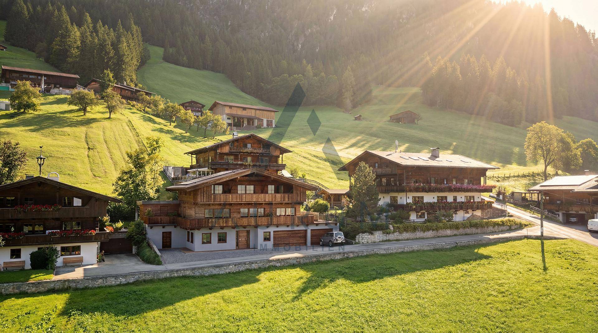 Alpines Anwesen mit mehreren Gebäuden, umgeben von grünen Wiesen und majestätischen Bergen.