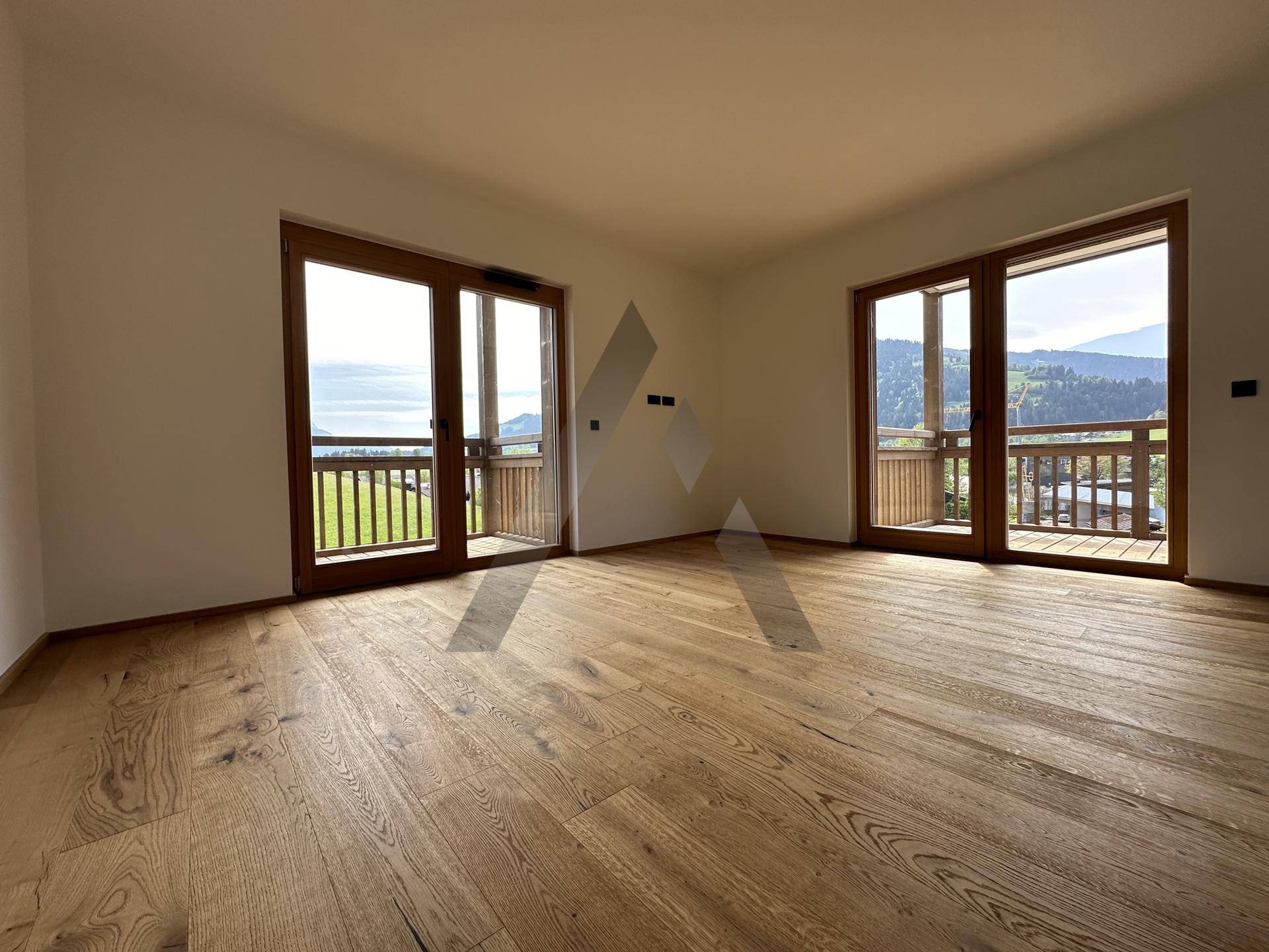 Helles Schlafzimmer mit Holzboden und zwei Balkonzugängen, bietet einen weiten Blick ins Grüne.