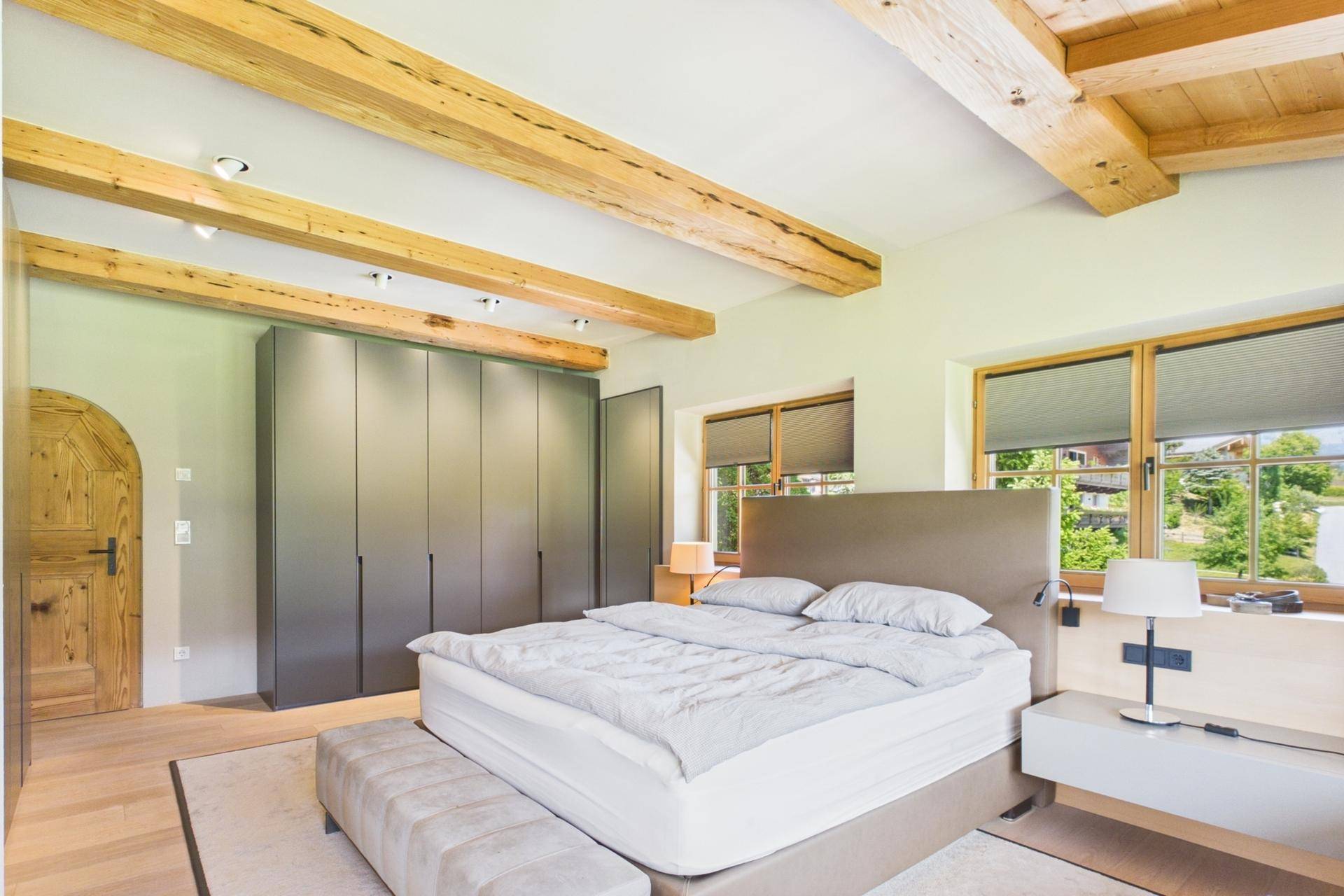 Modernes Schlafzimmer mit Holzbalken, großem Bett und Einbauschränken.