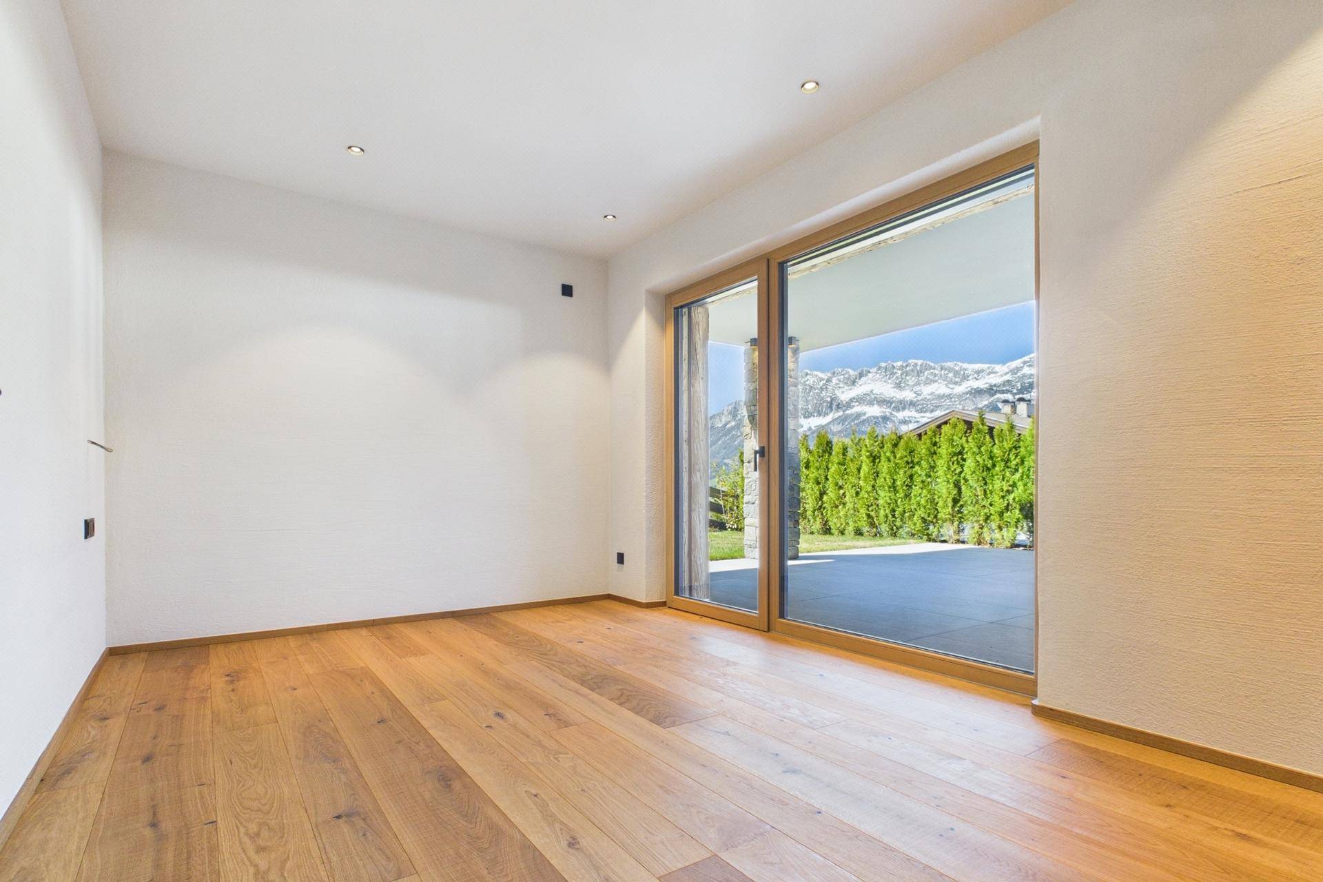 Heller Raum mit Holzboden und Zugang zu einer Terrasse mit Bergblick.