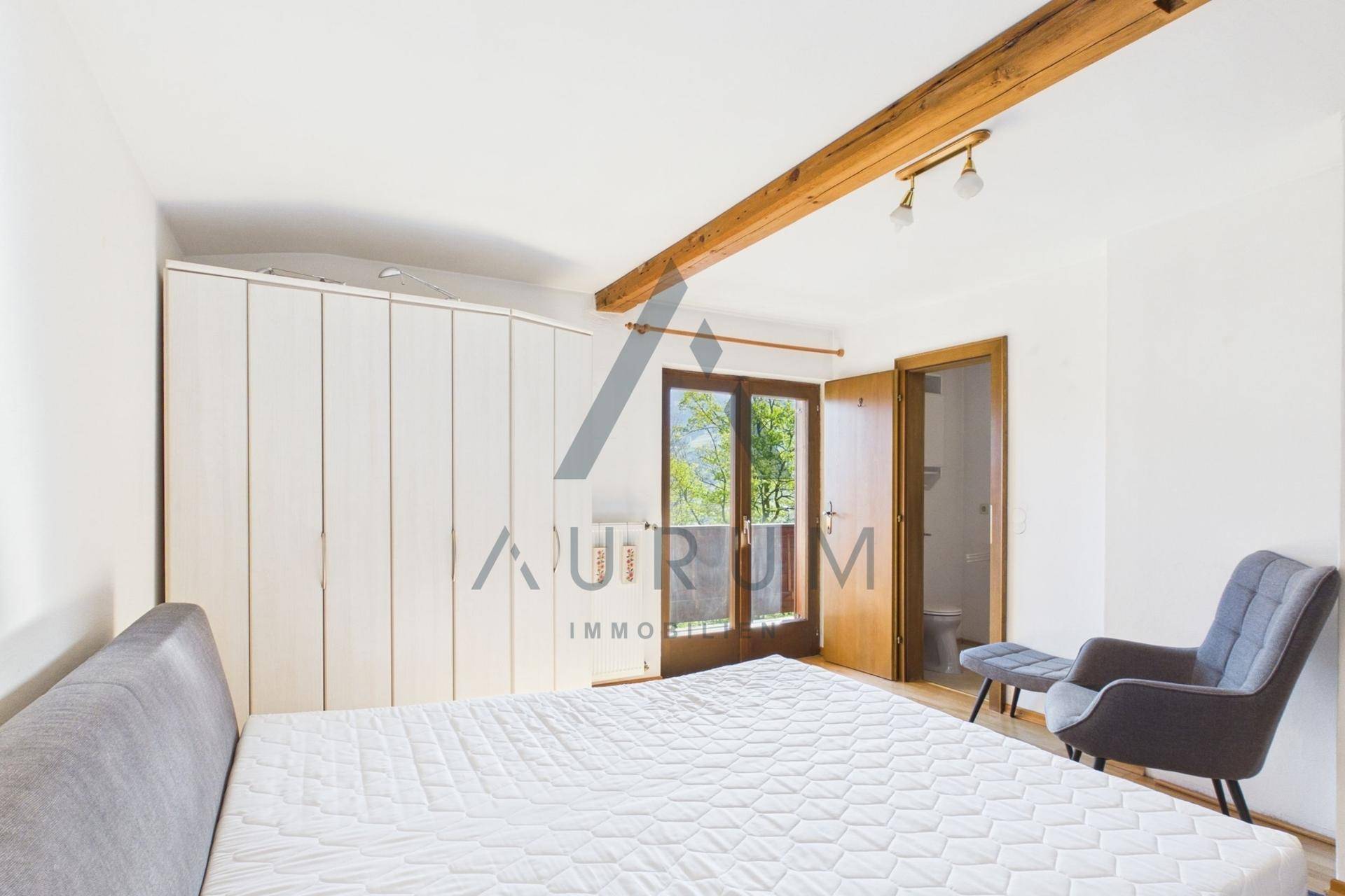 Helles Schlafzimmer mit Holzbalken, großem Kleiderschrank und Balkonzugang.