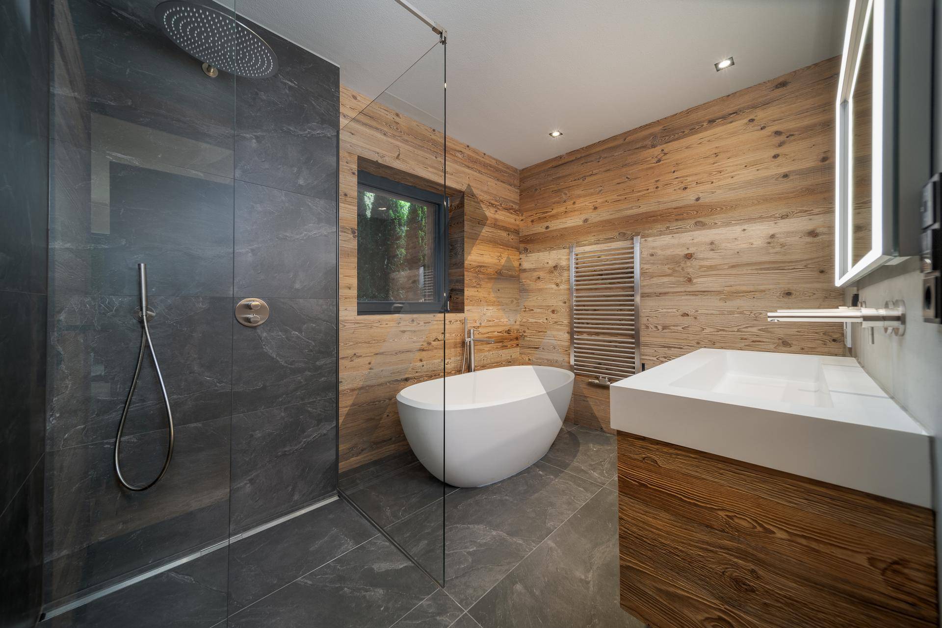 Elegantes Badezimmer mit freistehender Badewanne, großer Dusche und Holzwänden, sehr stilvoll.