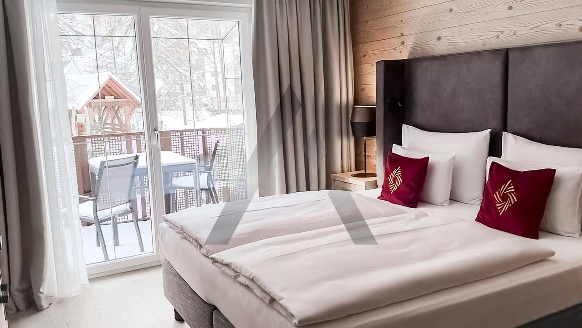 Gemütliches Schlafzimmer mit Doppelbett, Holzwand und Zugang zu einem verschneiten Balkon mit schöner Aussicht.