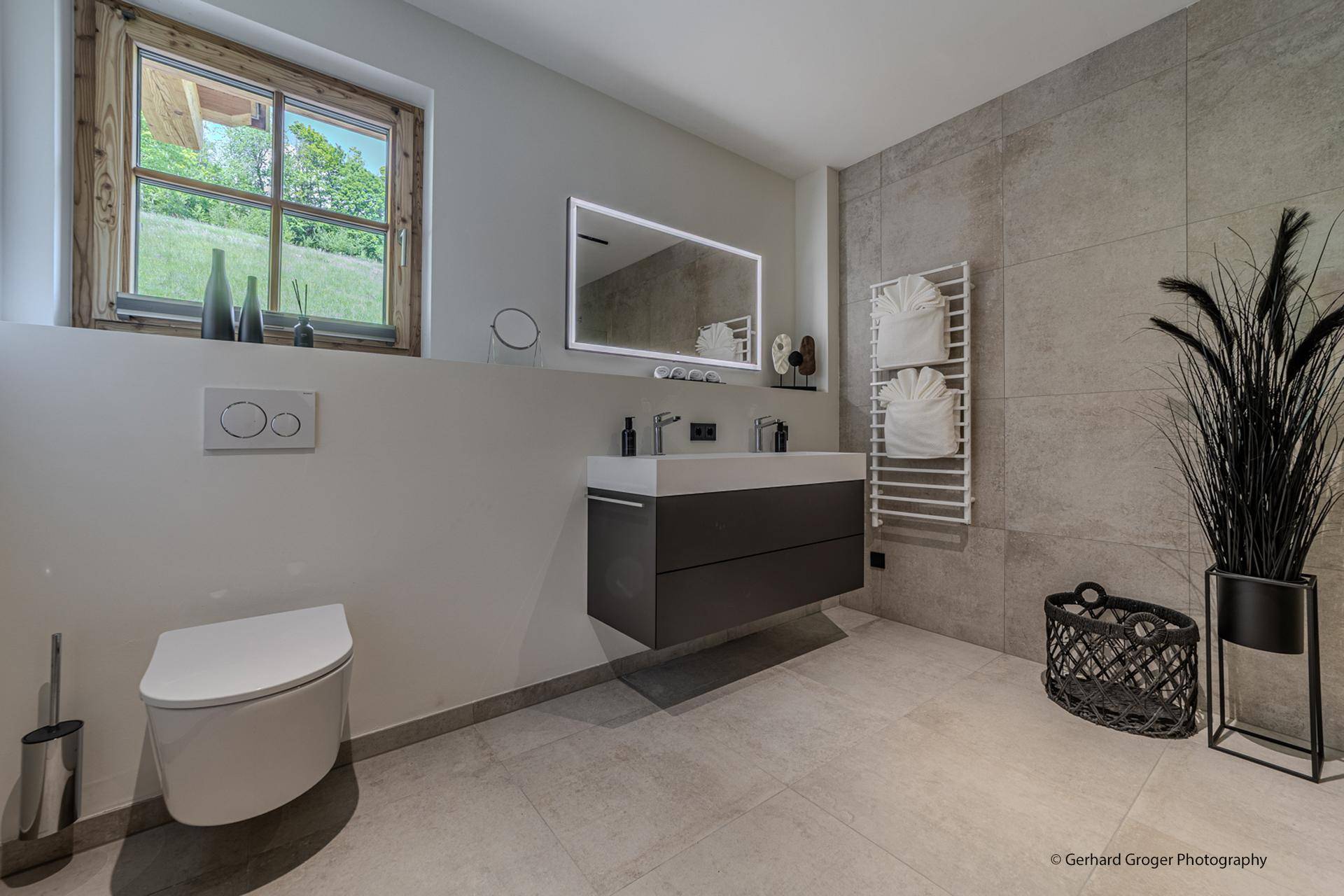 Helles Badezimmer mit modernem Doppelwaschbecken, Wand-WC und Fenster mit Grünblick.