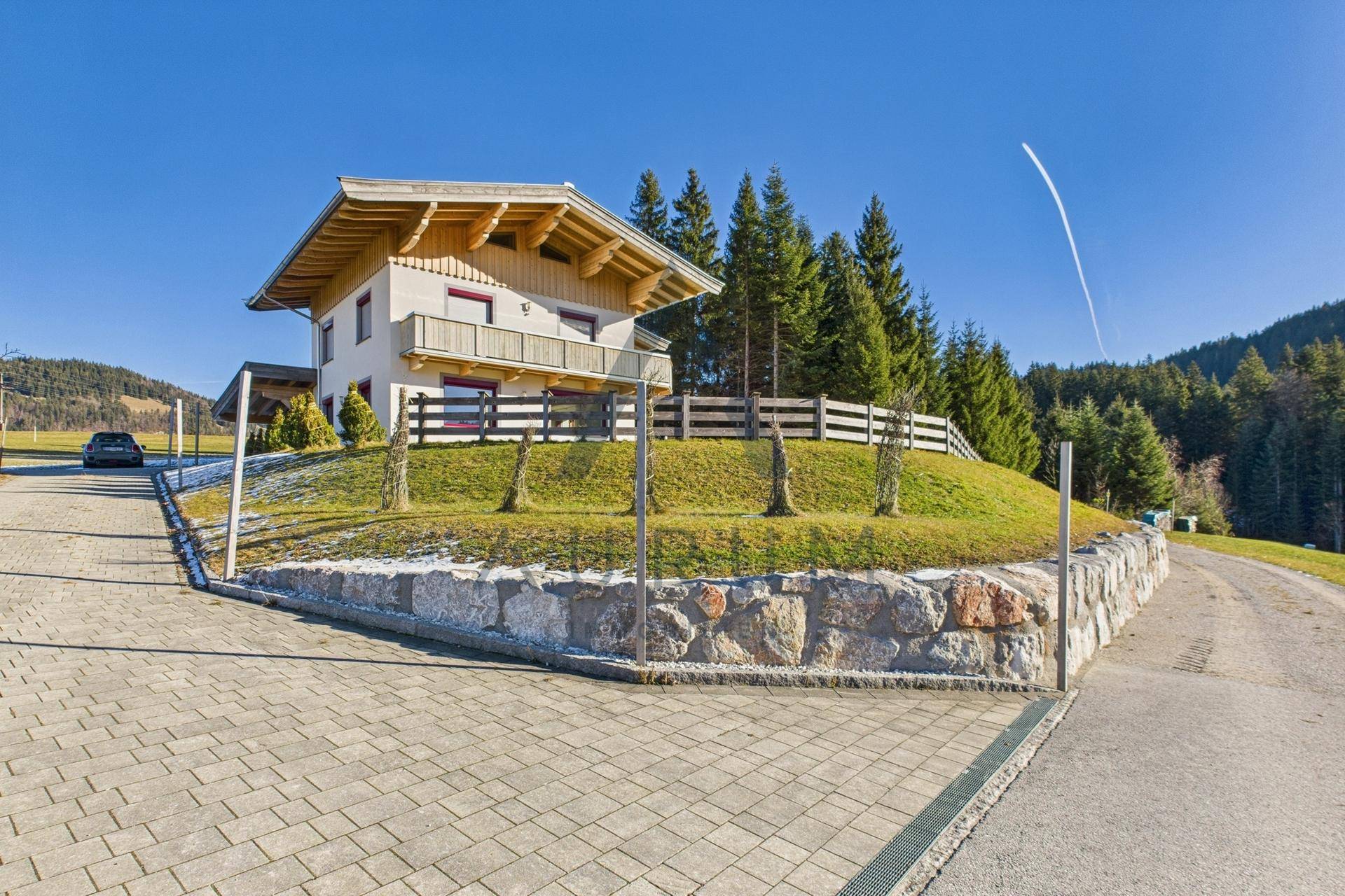Haus auf einem Hügel mit gepflasterter Auffahrt und Steinmauer, umgeben von Natur.