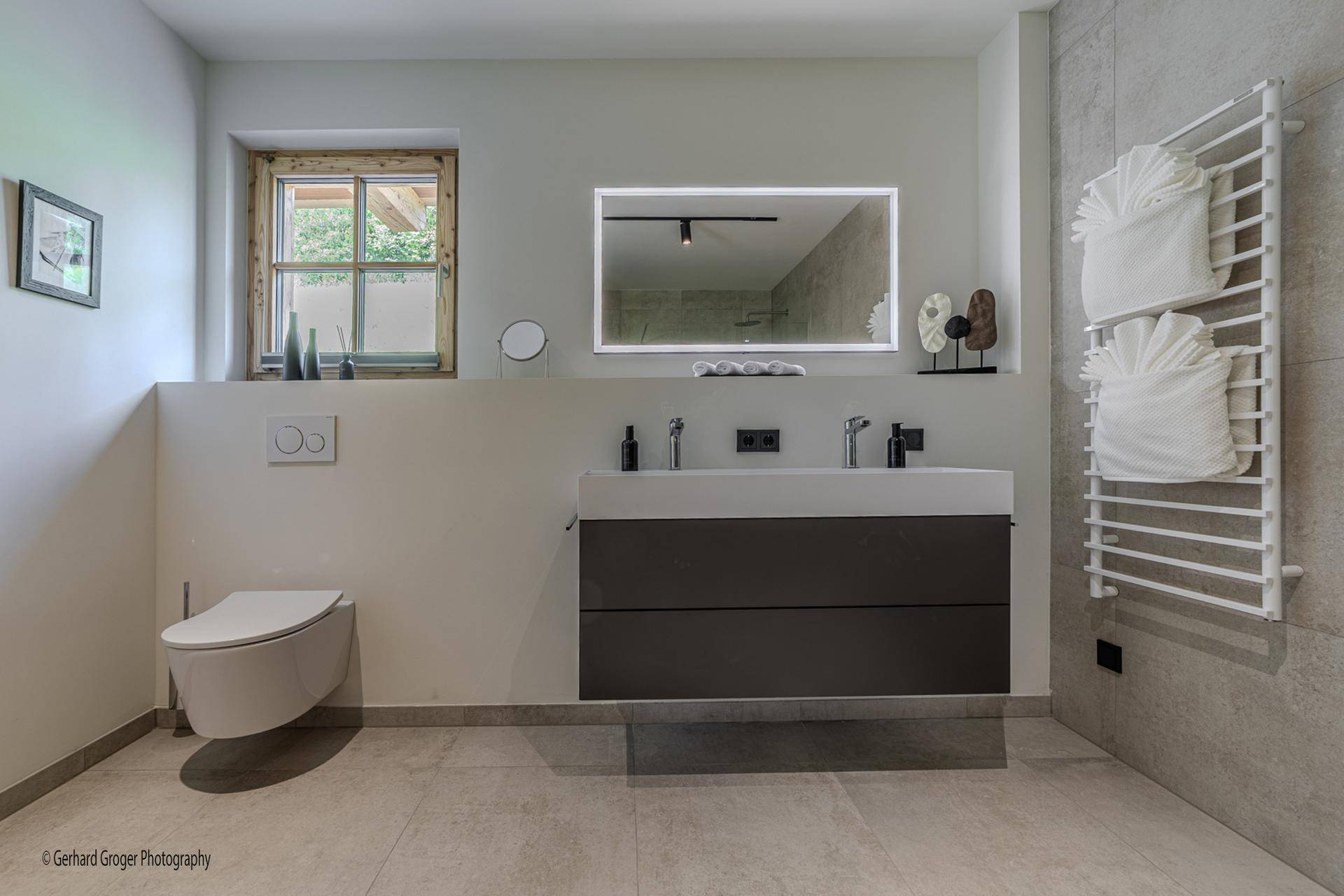 Modernes Badezimmer mit Doppelwaschbecken, Wand-WC und beheiztem Handtuchhalter.