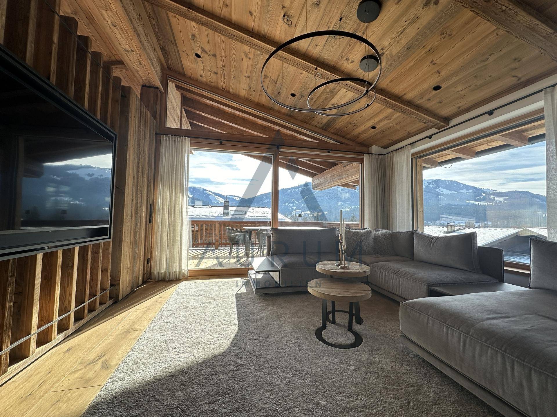 Gemütliches Wohnzimmer mit großem Sofa, Teppich und Zugang zum Balkon mit Panoramablick auf die Berge.