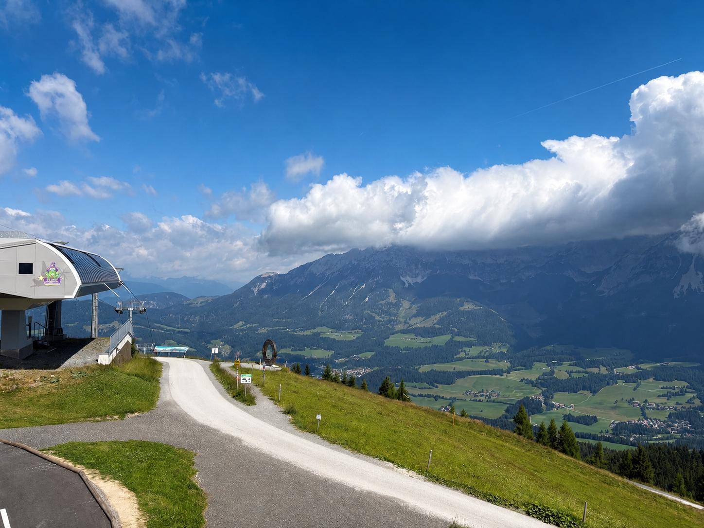 Panoramablick auf die majestätischen Berge und grüne Täler mit einer Seilbahnstation im Vordergrund.