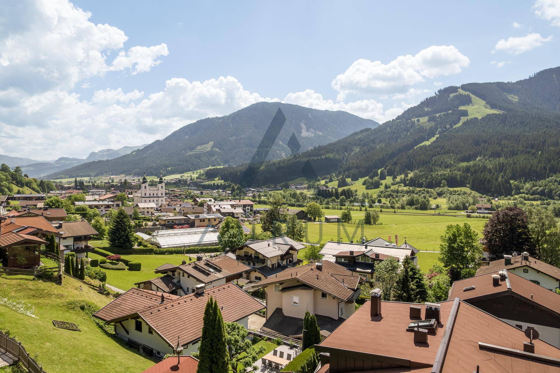 Weitläufiger Blick über ein charmantes Dorf mit Kirche und grünen Bergen im Hintergrund.