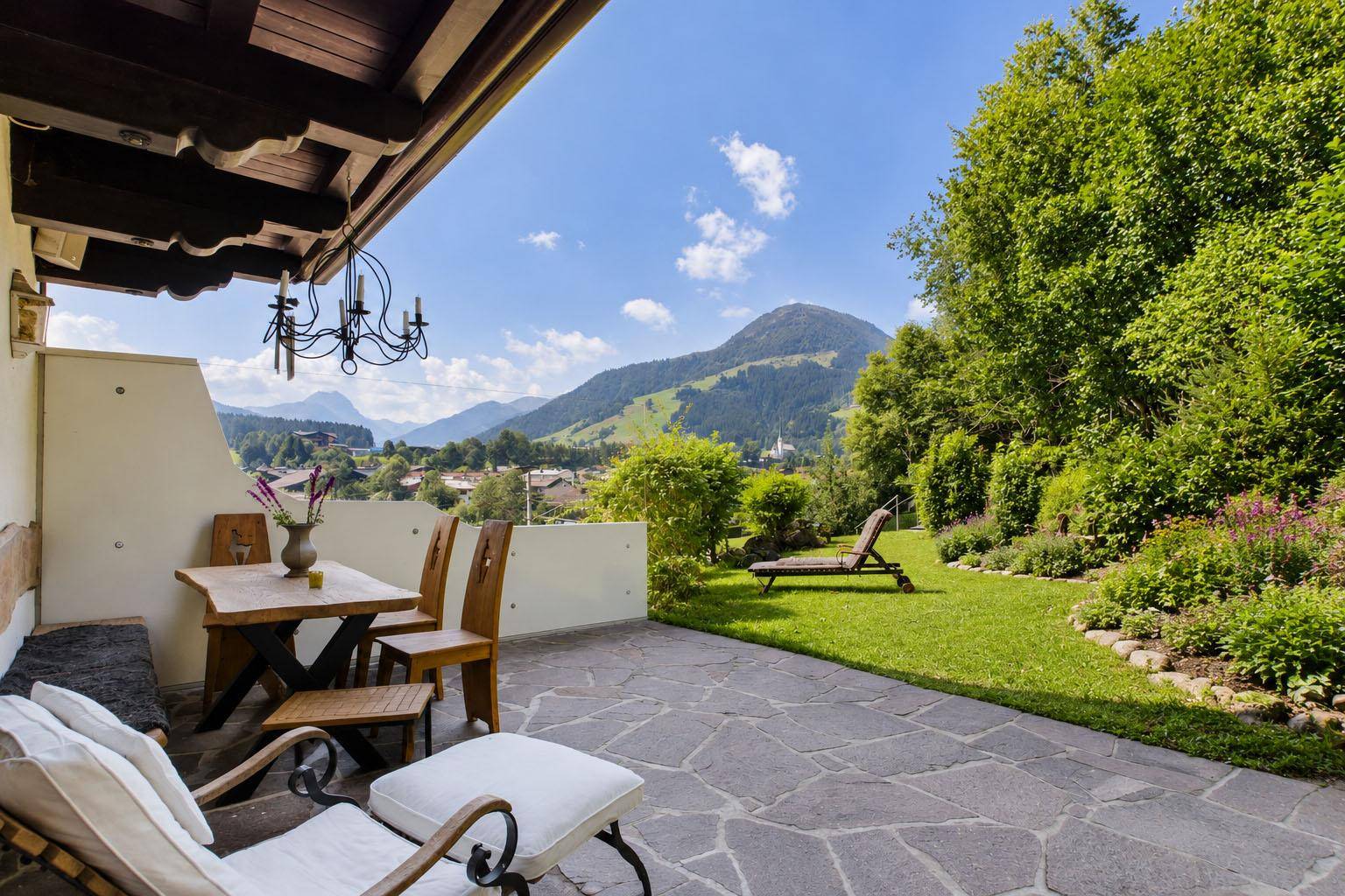 Große Steinterrasse mit Gartenmöbeln, Rasenfläche und herrlichem Bergblick.