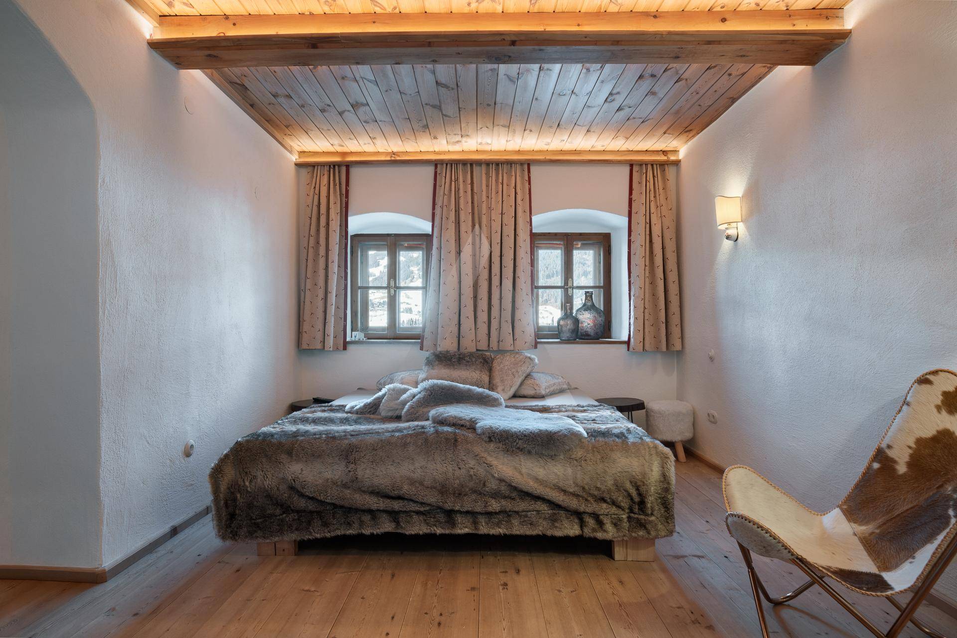 Gemütliches Schlafzimmer mit Holzbalkendecke, Holzboden und indirekter Beleuchtung.