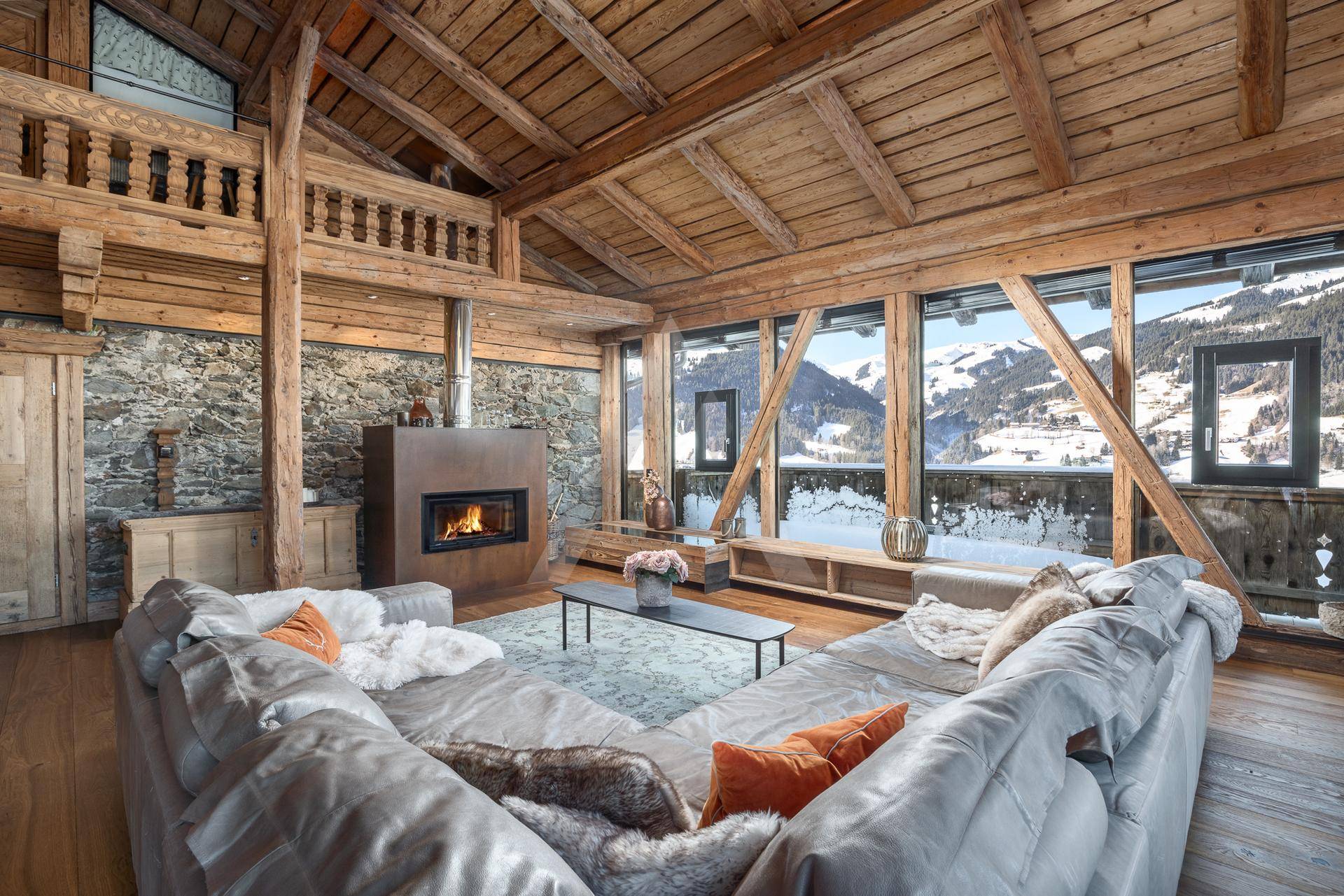Gemütliches Wohnzimmer mit Kamin, Steinwand und beeindruckendem Bergblick durch große Fenster.