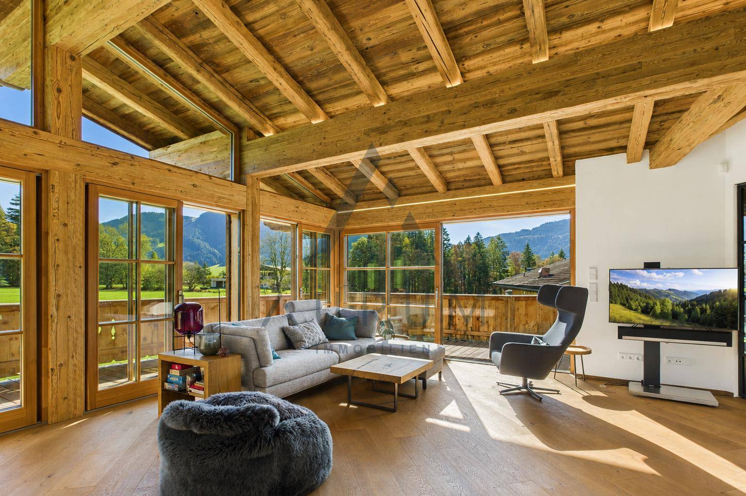 Lichtdurchflutetes Wohnzimmer mit Holzbalkendecke, großen Fenstern und Bergblick.