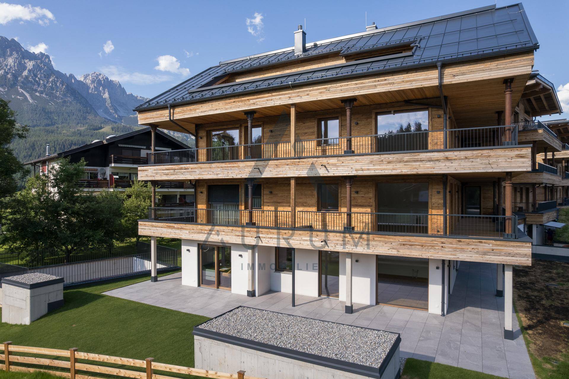 Erdgeschoss des modernen Holzgebäudes mit Zugang zu einer gepflasterten Terrasse und kleiner Grünfläche.