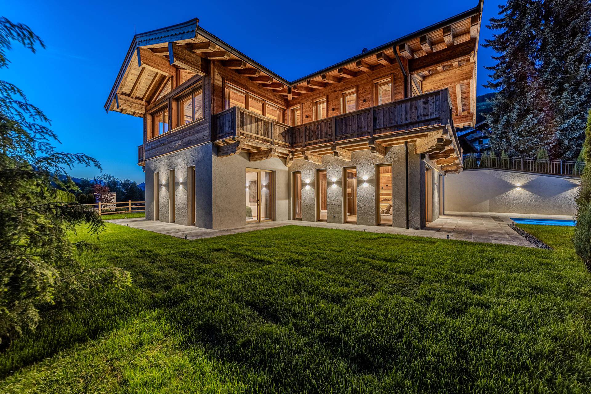 Moderne Chalet-Villa bei Dämmerung mit beleuchtetem Garten und kleinem Poolbereich.