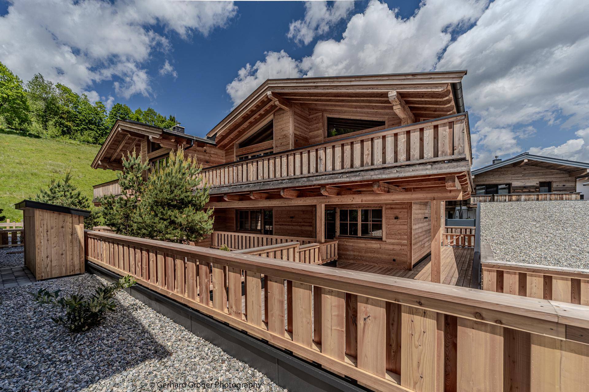 Modernes Holzchalet mit traditioneller Architektur und einem Kiesbereich im Vordergrund unter blauem Himmel.