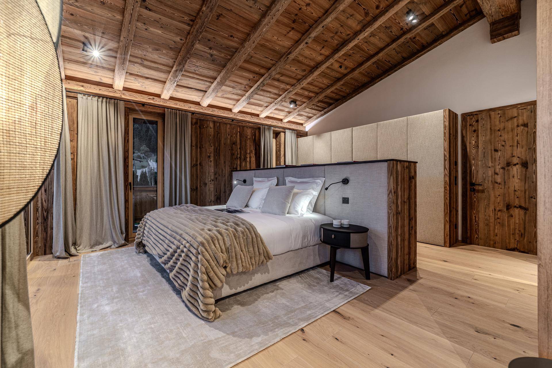 Gemütliches Schlafzimmer mit Holzbalkendecke, großem Bett und Blick auf die Natur.