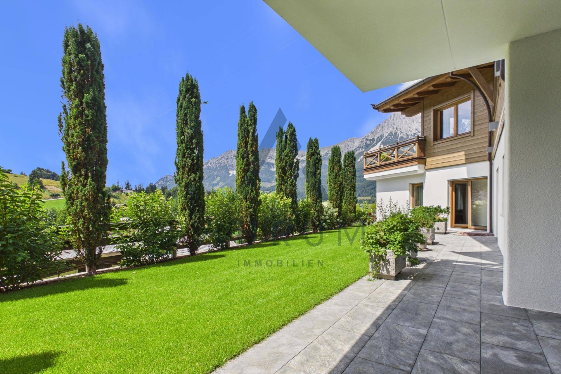 Gepflegter Gartenbereich mit Rasenfläche, Terrasse und Blick auf die umliegende Berglandschaft.