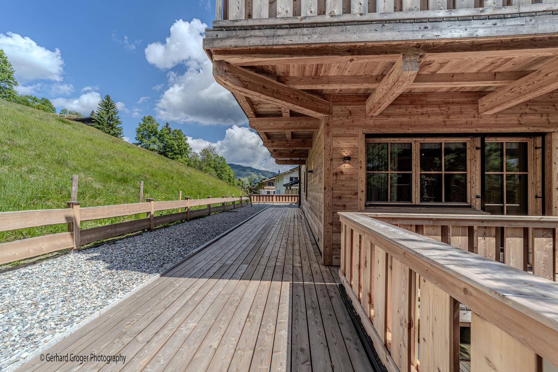 Lange Holzterrasse entlang des Gebäudes mit Blick auf die grüne Hügellandschaft.