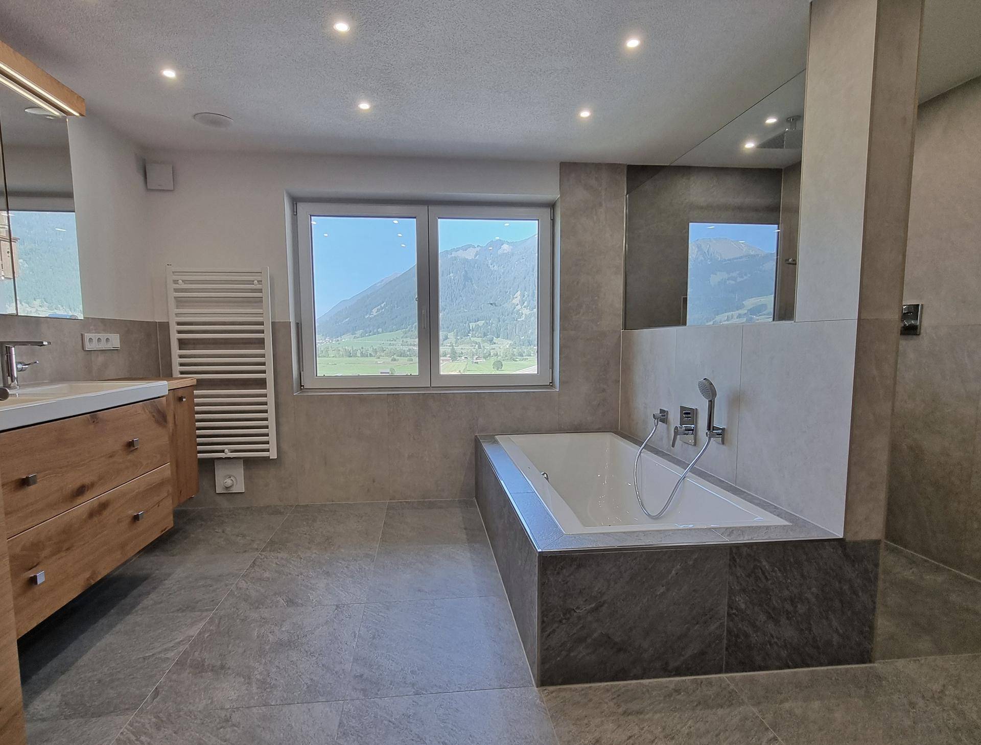 Modernes Badezimmer mit Badewanne, großem Fenster und beeindruckendem Bergblick.