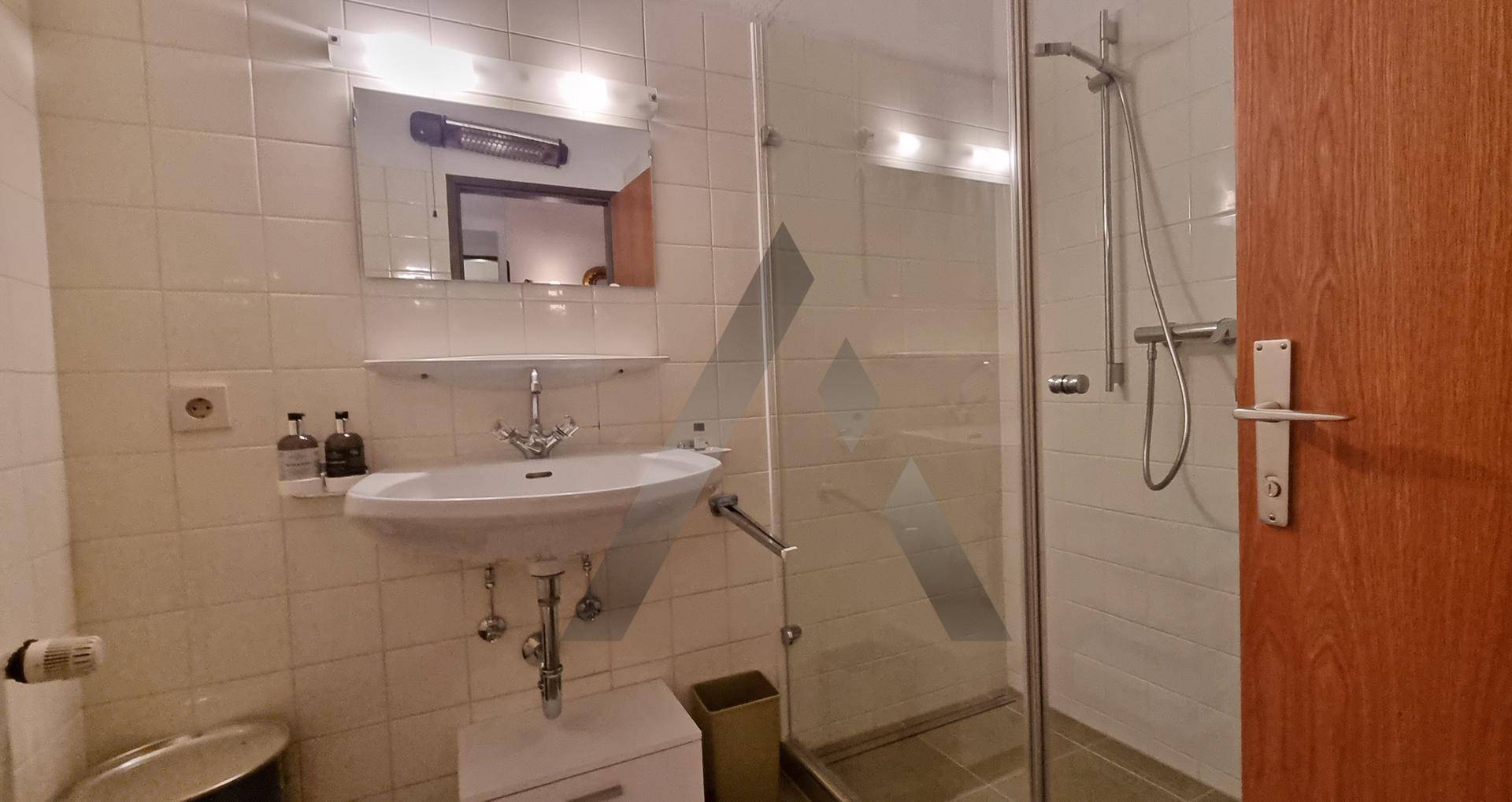 Badezimmer mit Dusche, Waschbecken und weißen Fliesen, funktional und hell gestaltet
