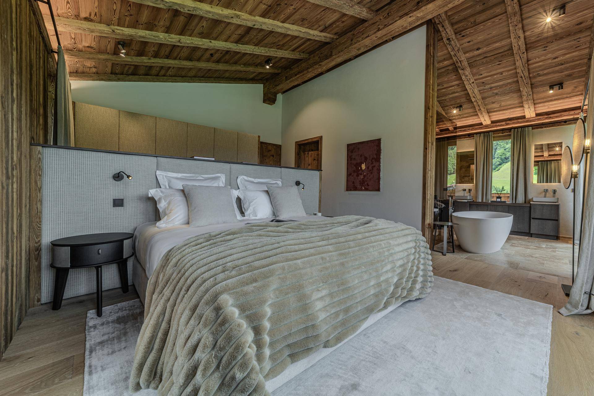 Geräumiges Schlafzimmer mit Holzbalkendecke, großem Bett und offener Badewanne mit Bergblick.