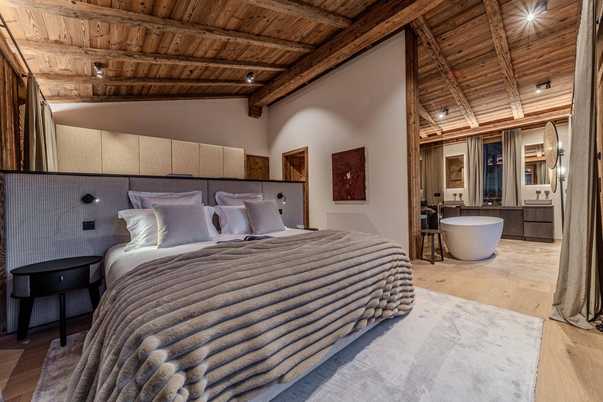 Geräumiges Schlafzimmer mit Holzbalkendecke, großem Bett und offener Badewanne mit Bergblick.