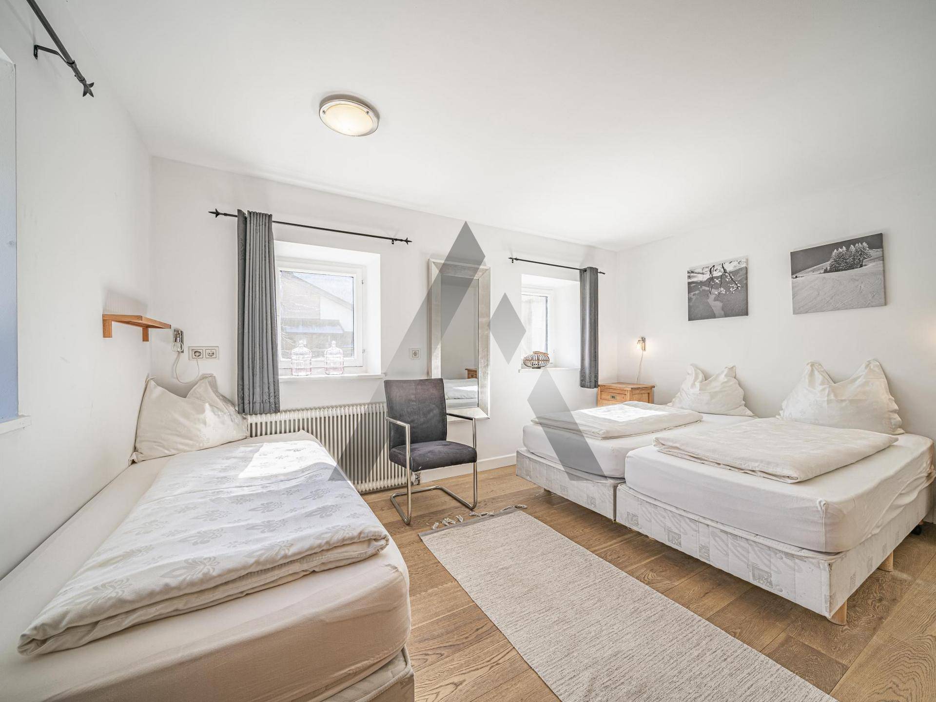 Helles Schlafzimmer mit drei Einzelbetten, Holzfußboden und Fenstern für natürliches Licht.