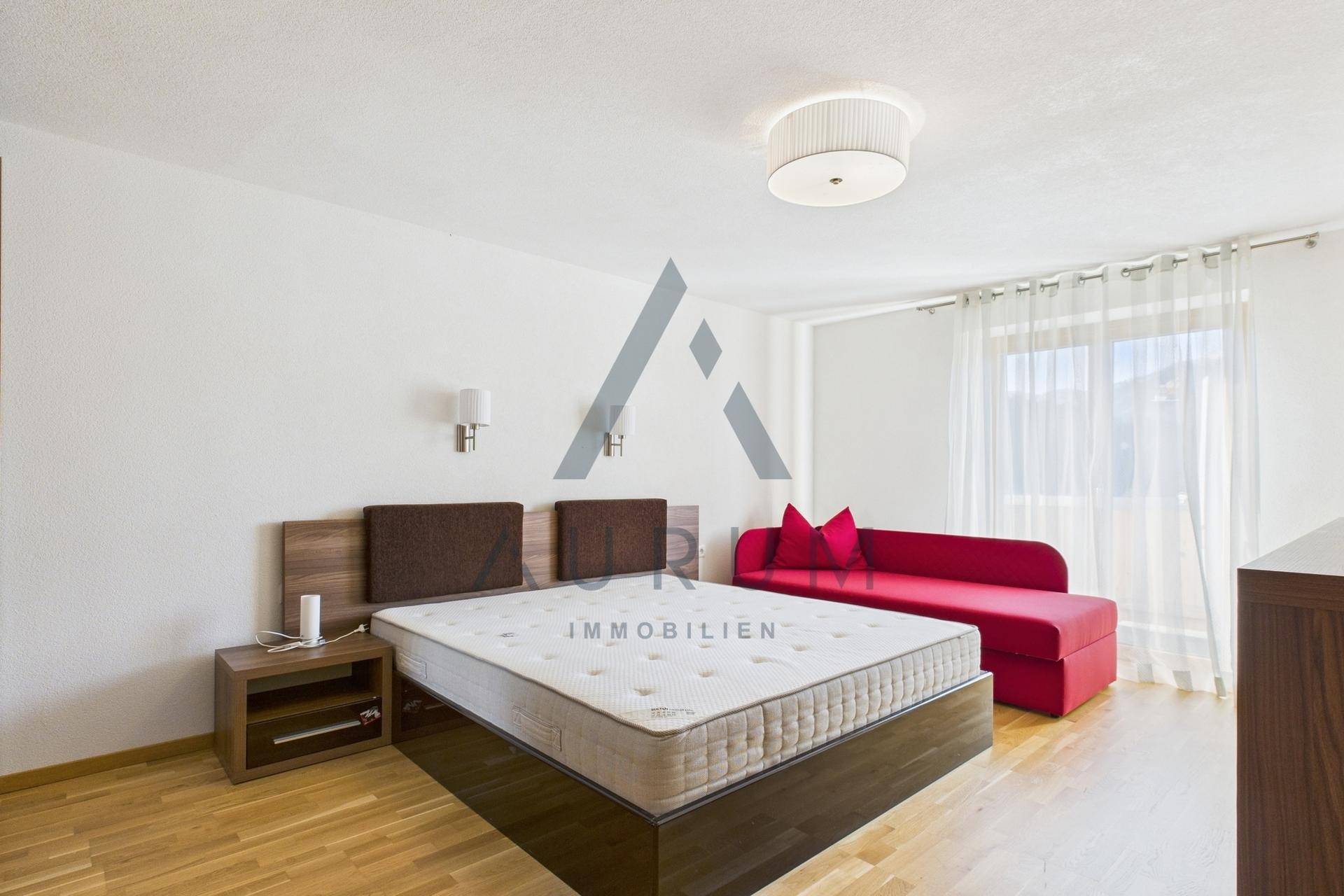 Gemütliches Schlafzimmer mit Doppelbett, Holzboden und einem roten Sofa als Farbakzent.